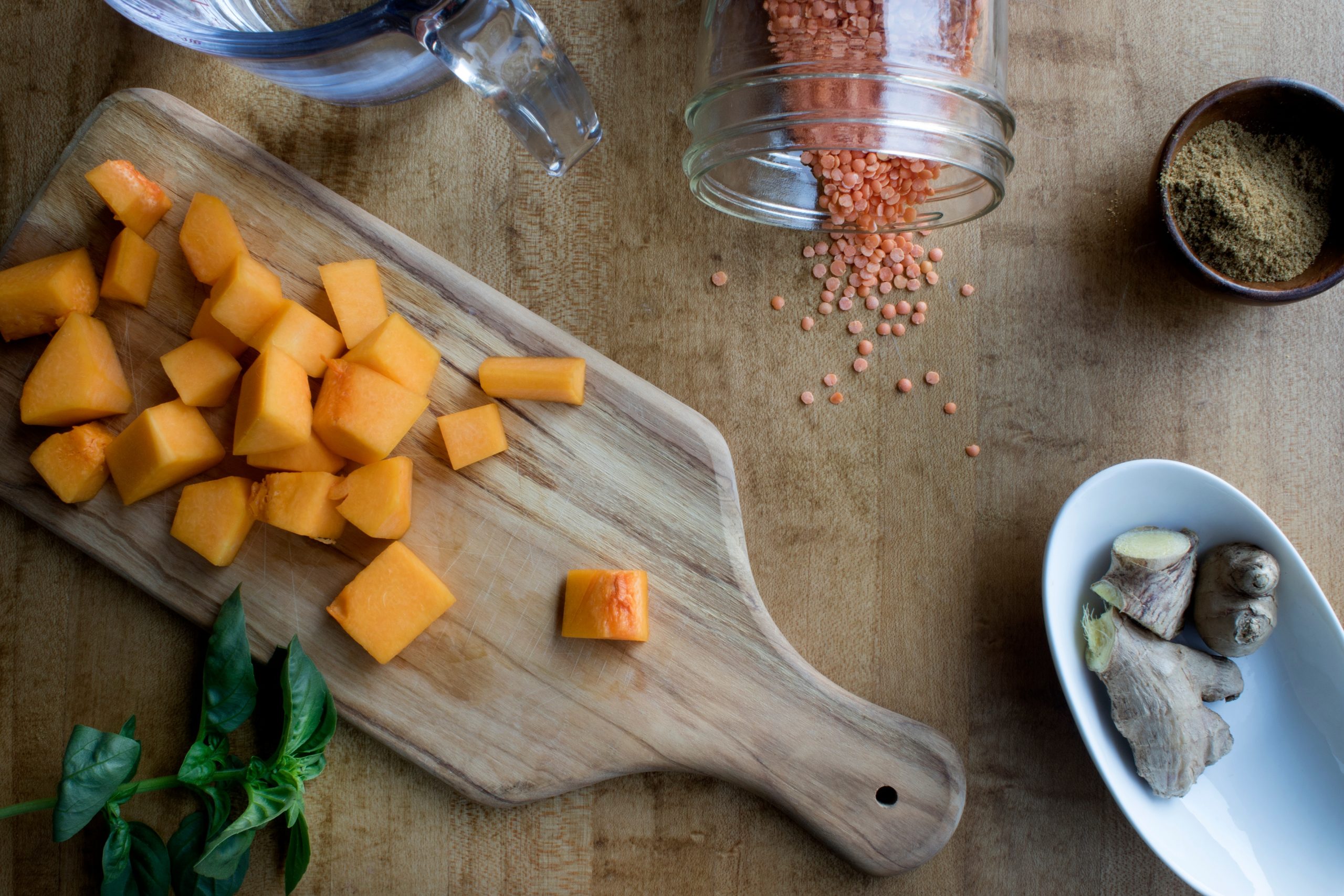 Cutting board with cut squash, a bowl with fresh ginger, mason jar with lentils spilling out and a cup of spice powder. 