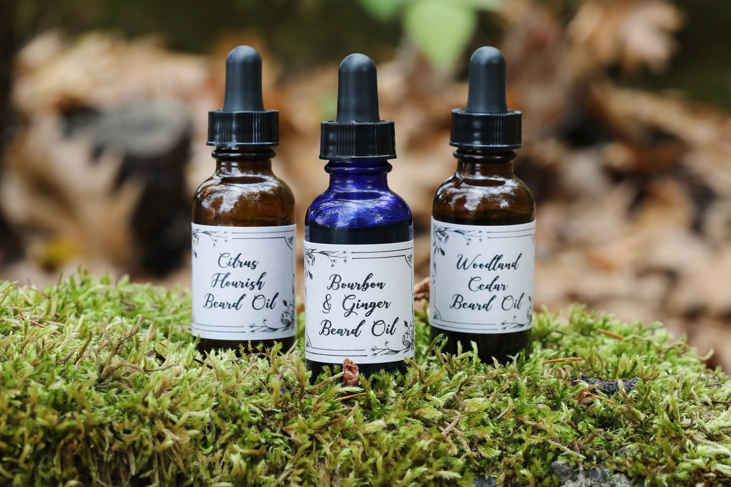 Three displayed colorful dropper top bottles sitting on moss. 