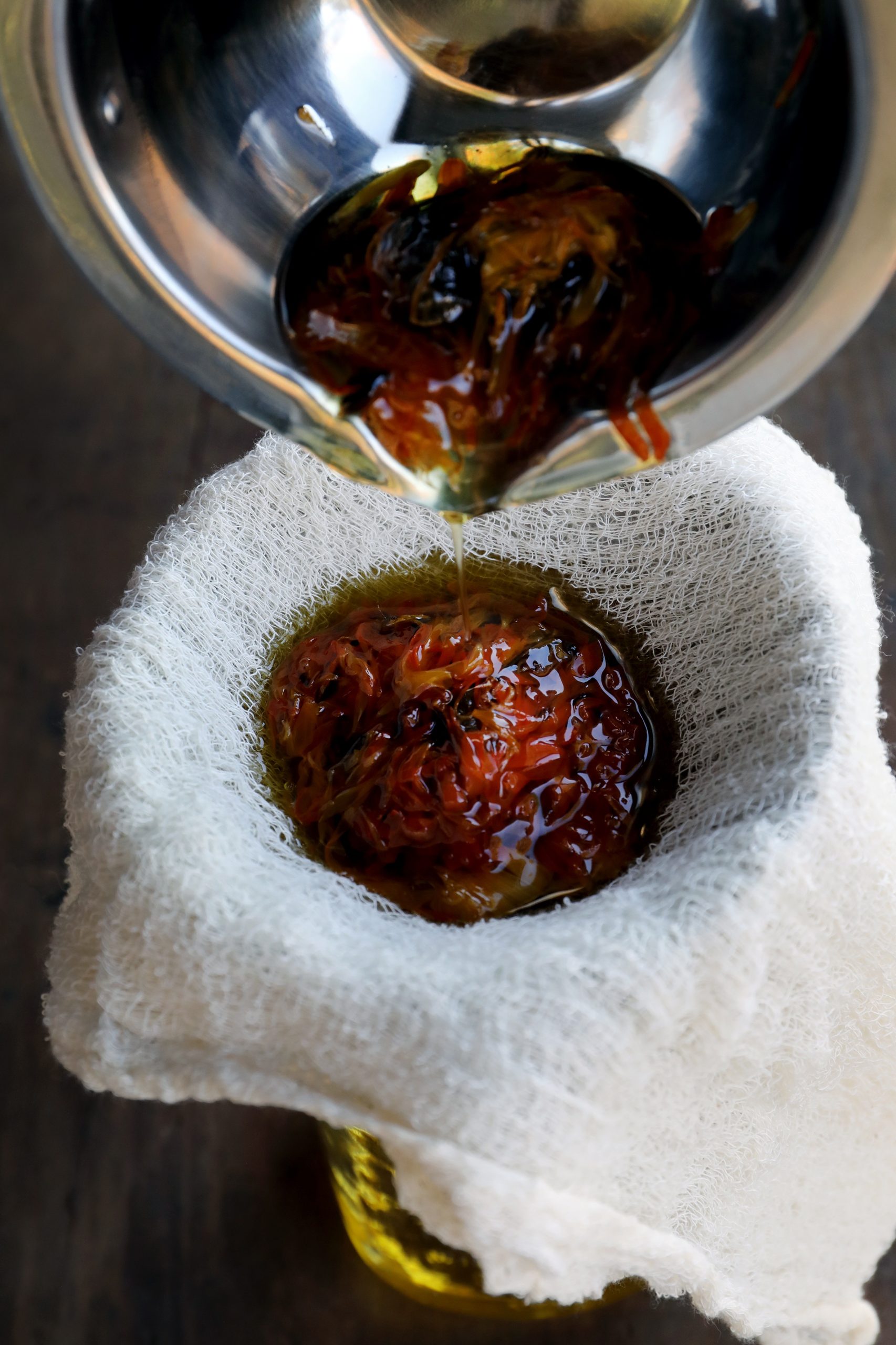 Pouring herb-infused oil through cheesecloth