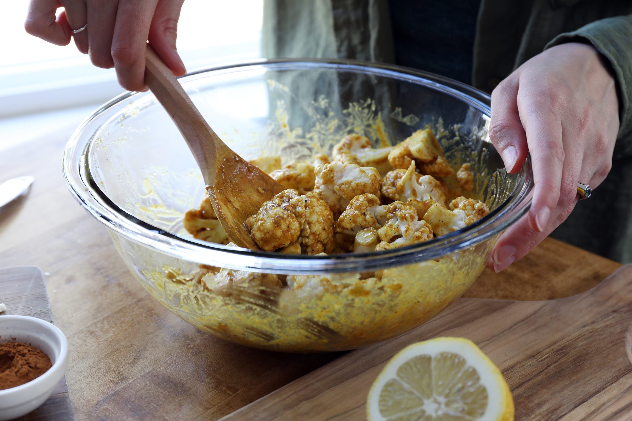 Hands holding wooden spoon and glass mixing bowl stirring cauliflower into curry blend Hands holding wooden spoon and glass mixing bowl stirring cauliflower into curry blend