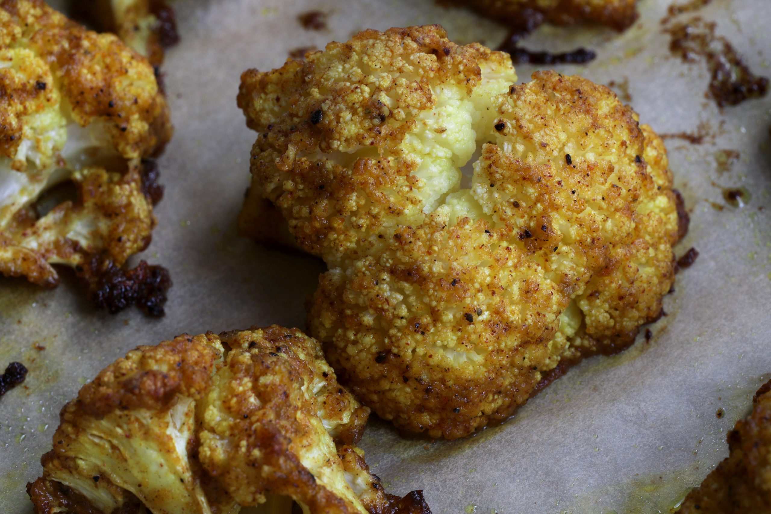 Close up photo of pieces of curried cauliflower on parchment paper on baking sheet Close up photo of pieces of curried cauliflower on parchment paper on baking sheet