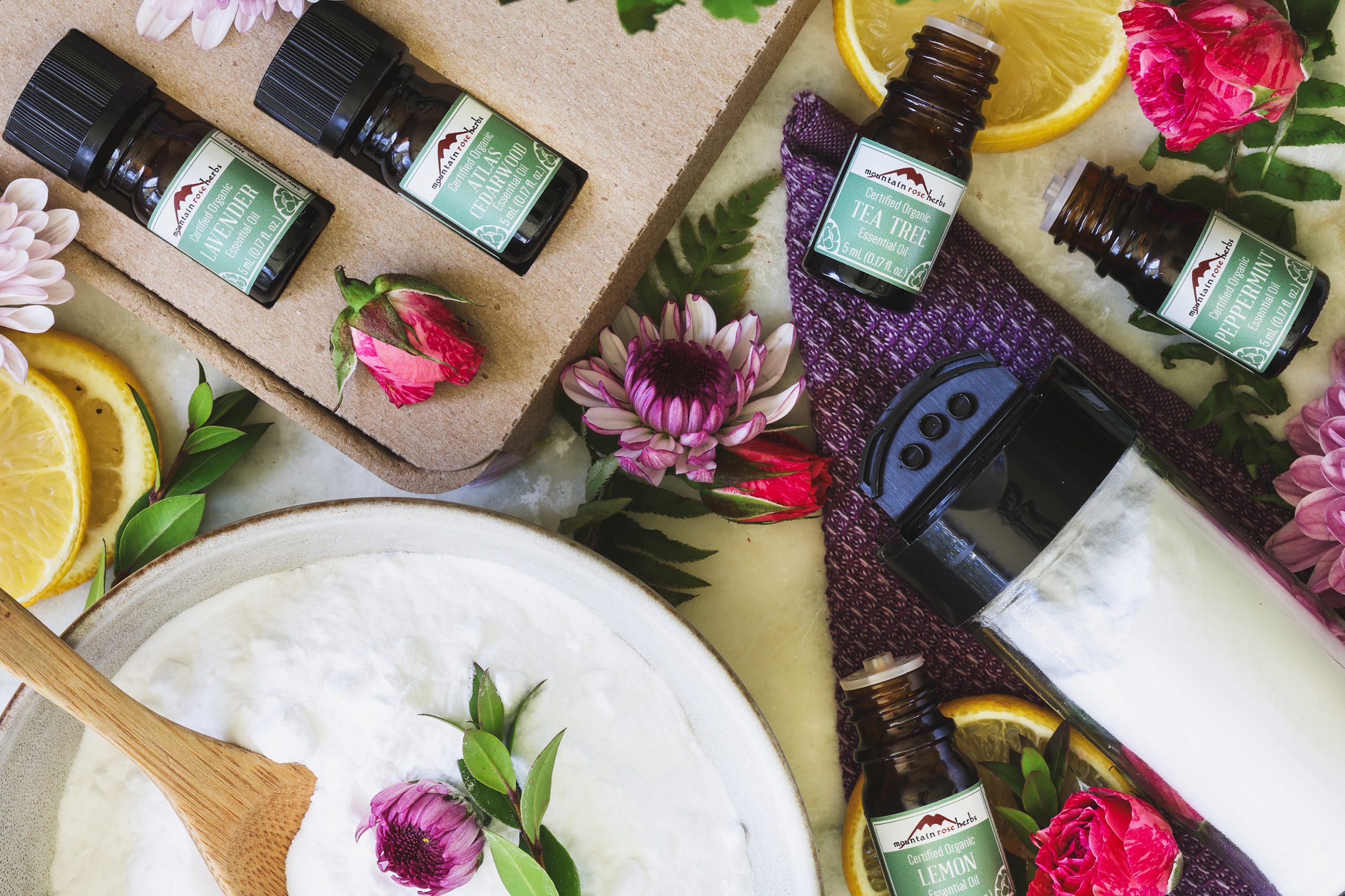 An overhead shot of scrub powder in a bowl with essential oils and shaker bottle next to it