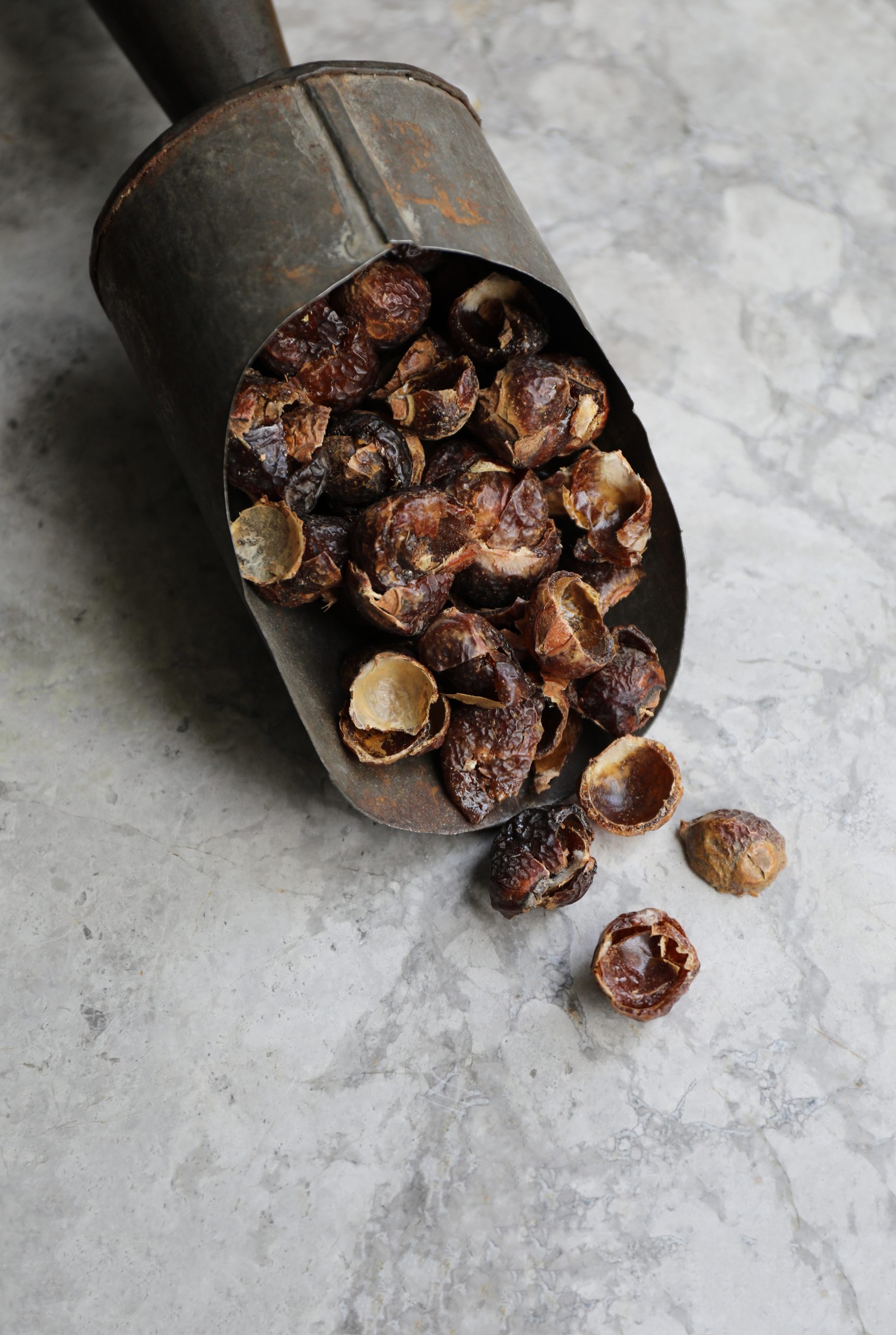 Seeded soap nuts in old metal scoop on marble counter