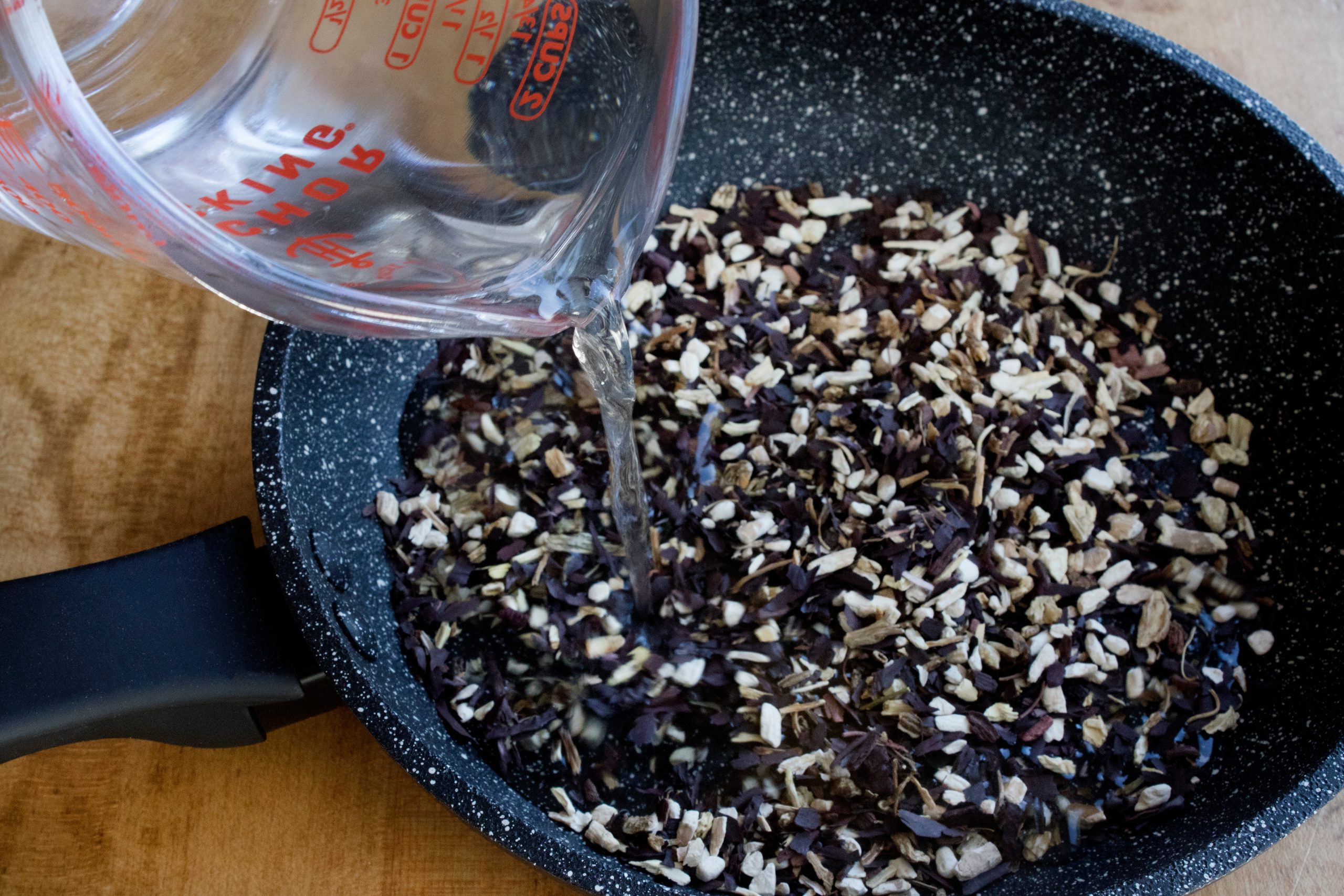 Dried cut roots in for saut pan with measuring cup pouring water.