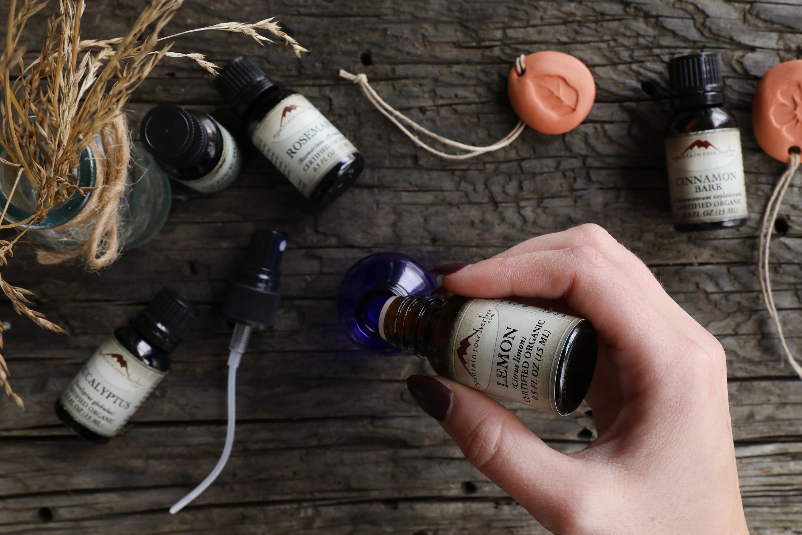 Hand pouring essential oil into cobalt glass bottle with other essential oils displayed on rustic wood.