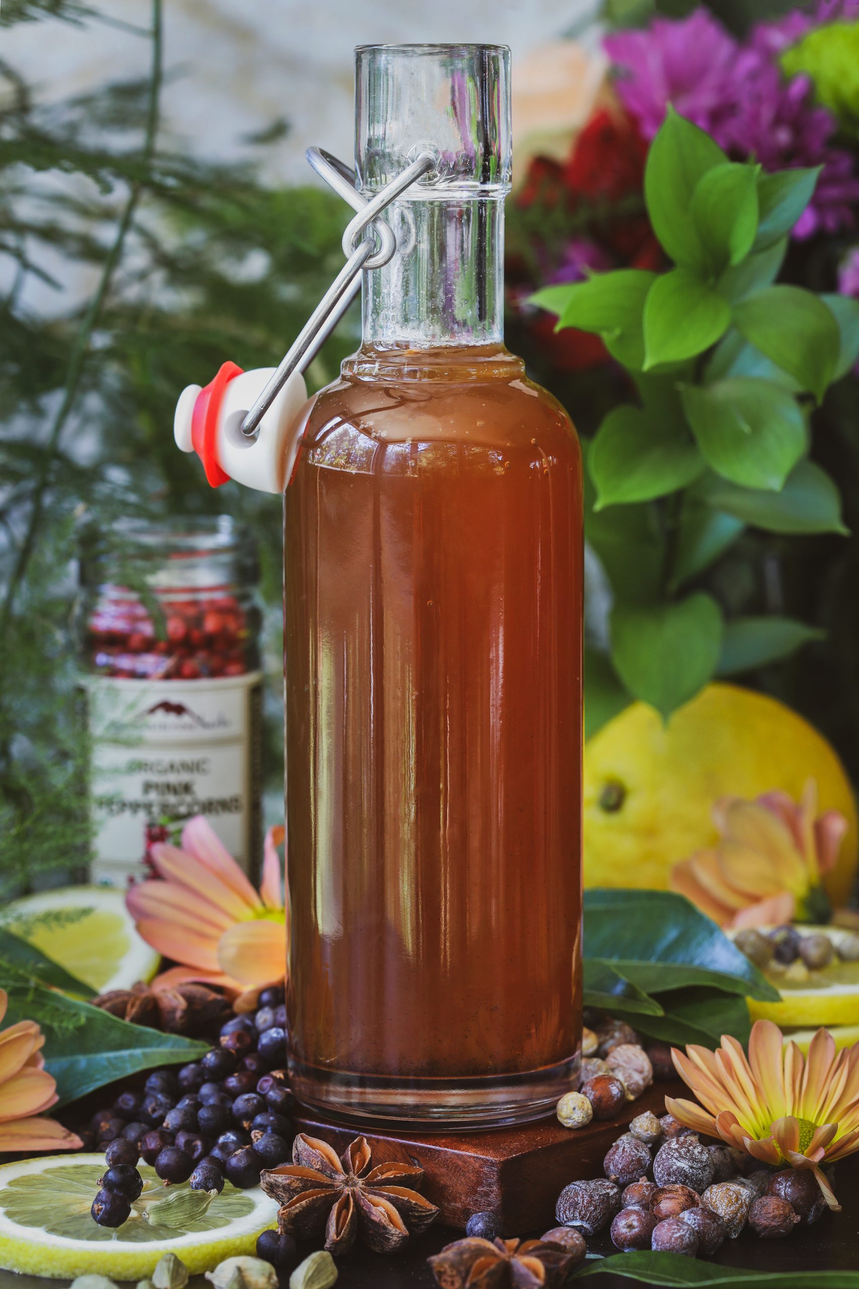 A tall ar of gin simple syrup sits with juniper and cedar berries and flowers