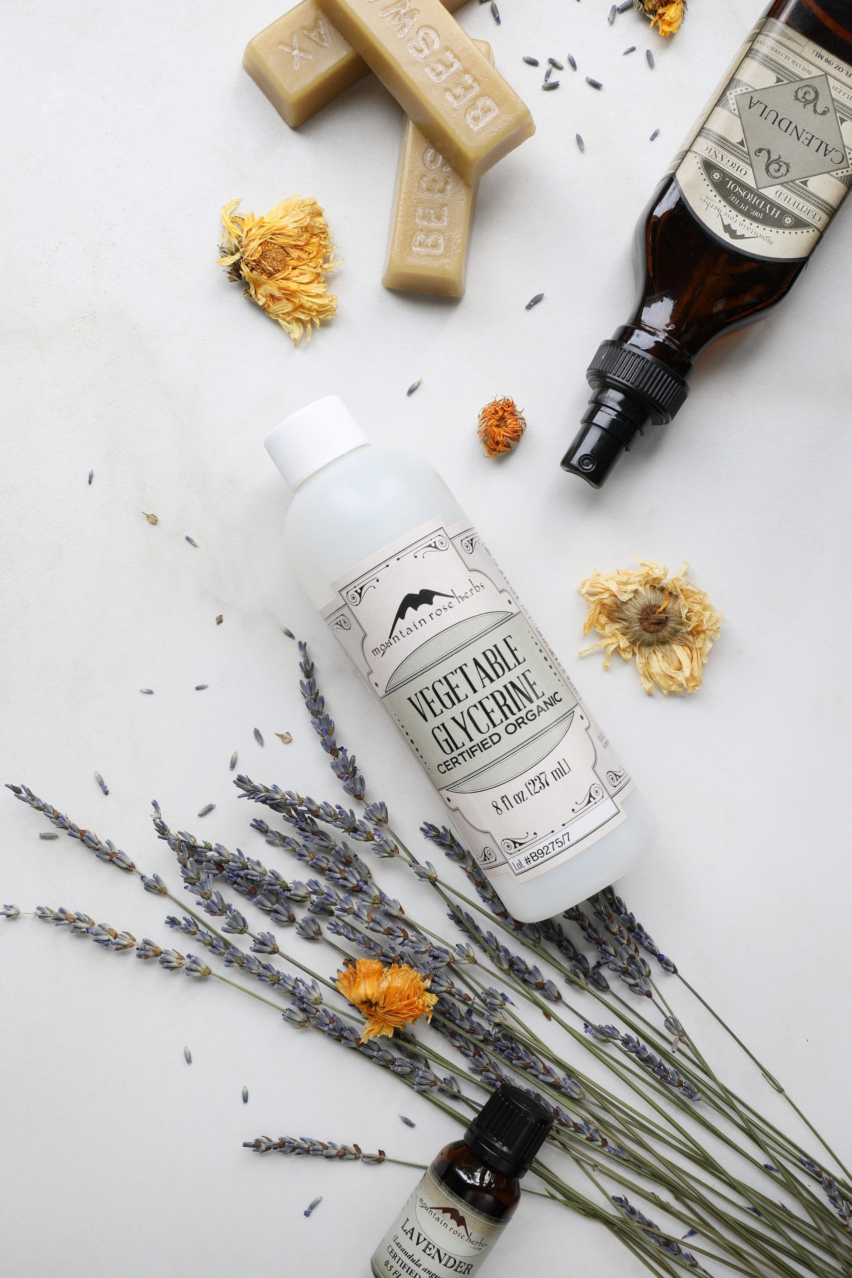 8 oz Mountain Rose Herbs vegetable glycerine on white background with dried lavender beeswax blocks and calendula hydrosol