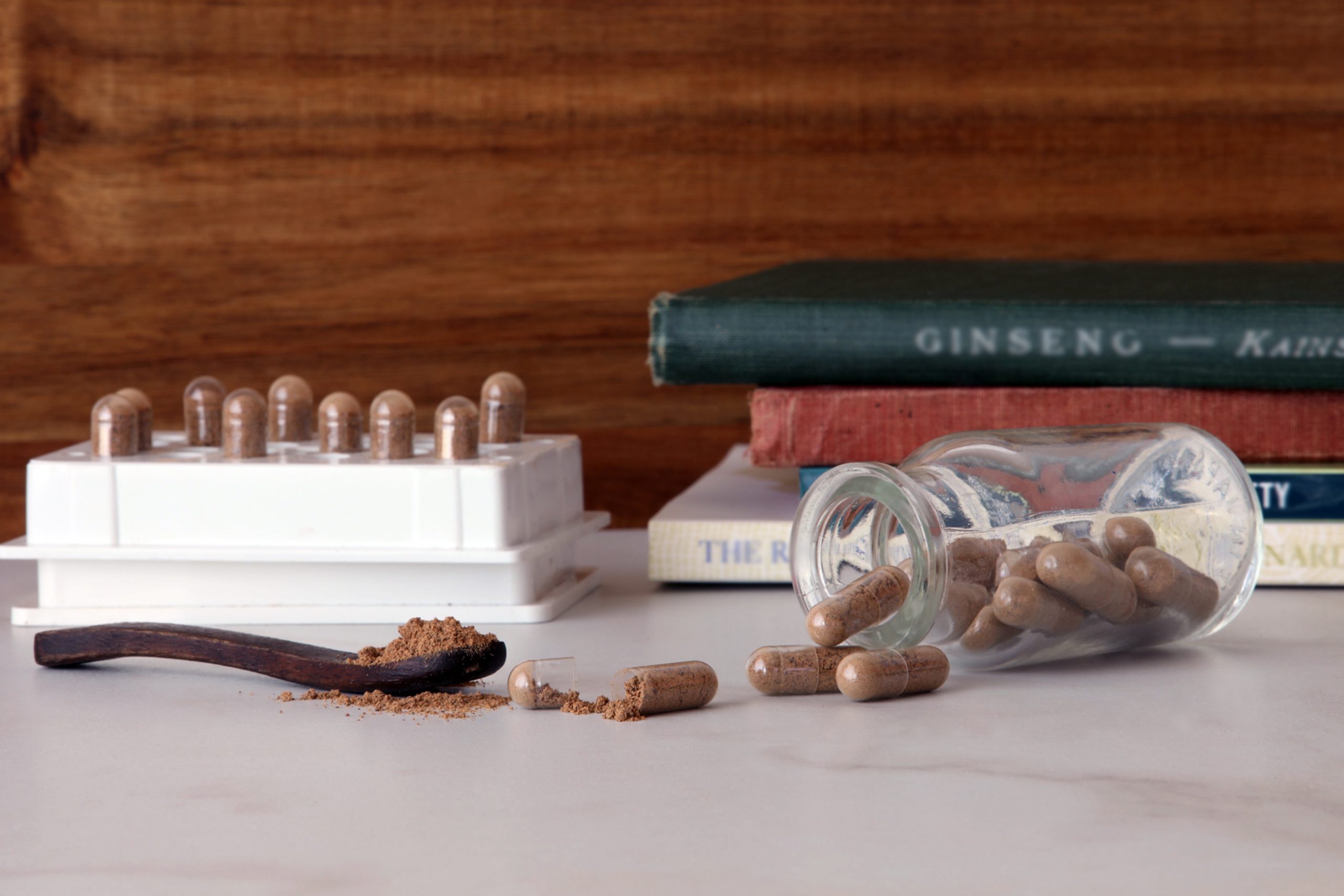 Jar of guarana capsules and guarana seed powder on counter next to capsule machine and books