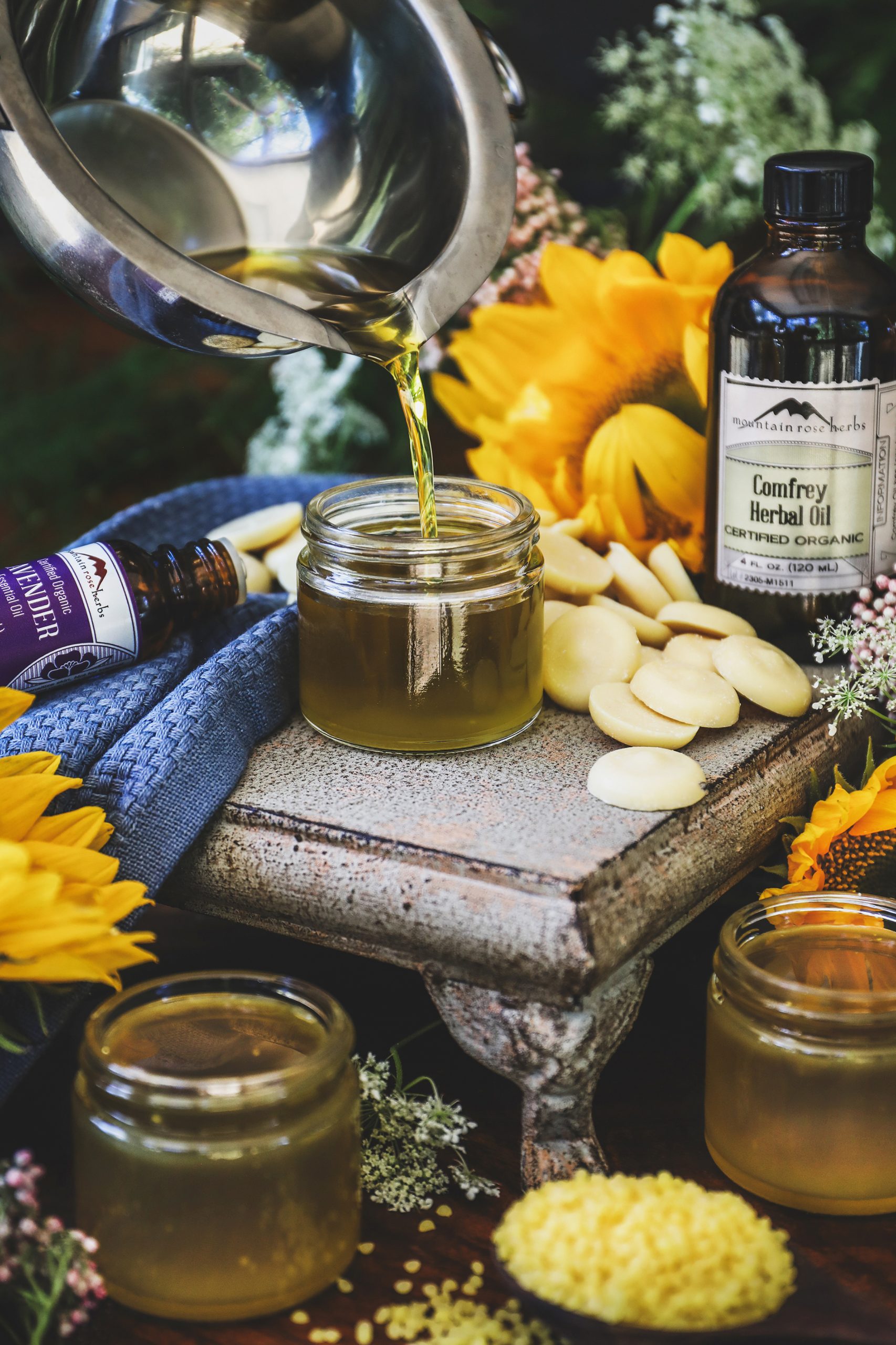 A comfrey oil salve being poured from a double boiler into a jar with ingredients nearby