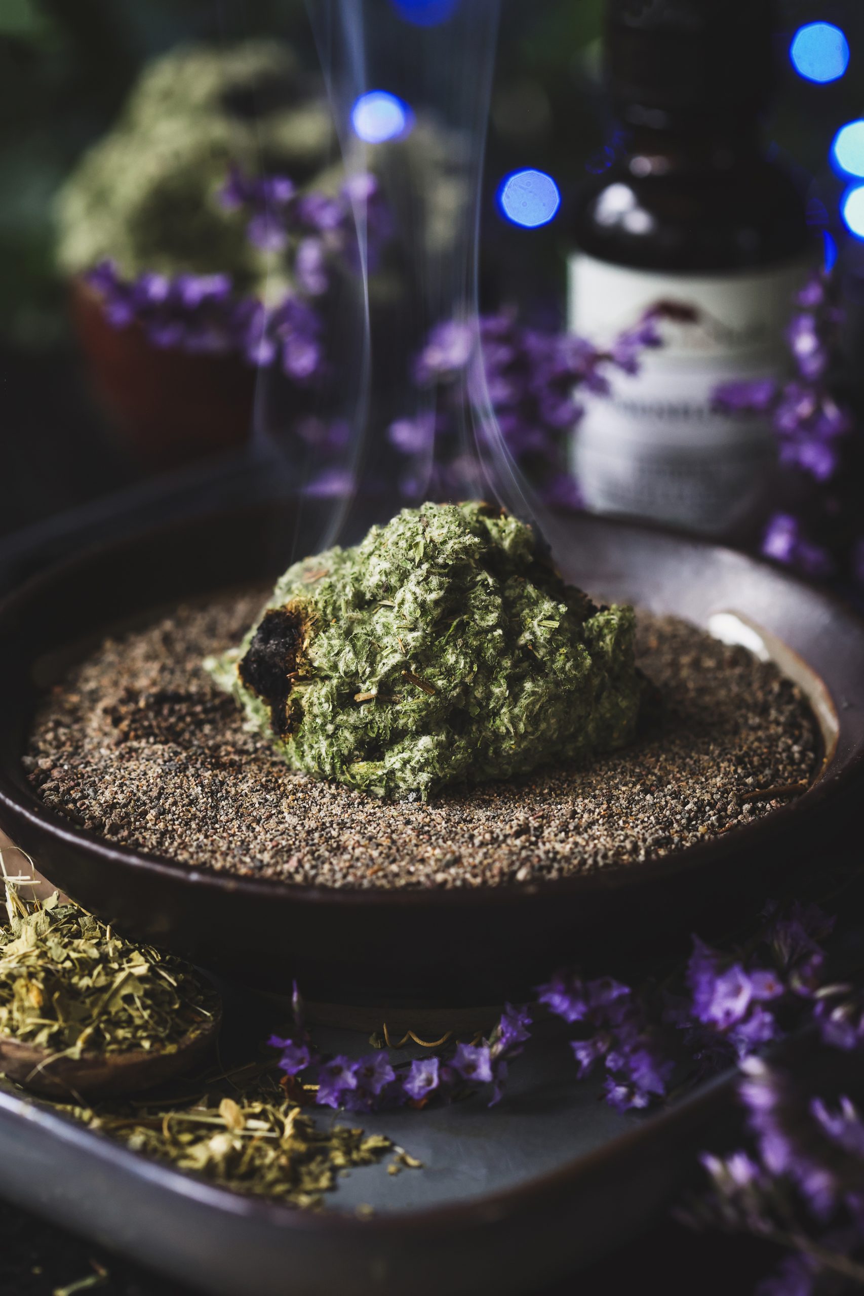 A small pile of dried mugwort in a dish of sand smokes as it is burned