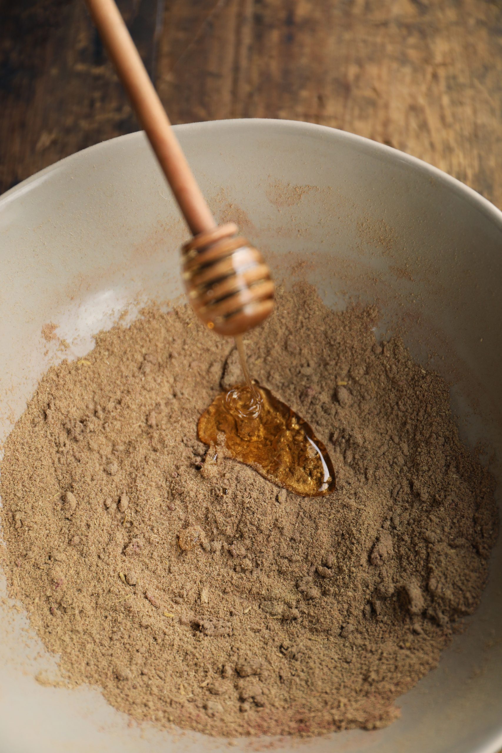 Drizzling honey into a bowl of tan powdered herbs.