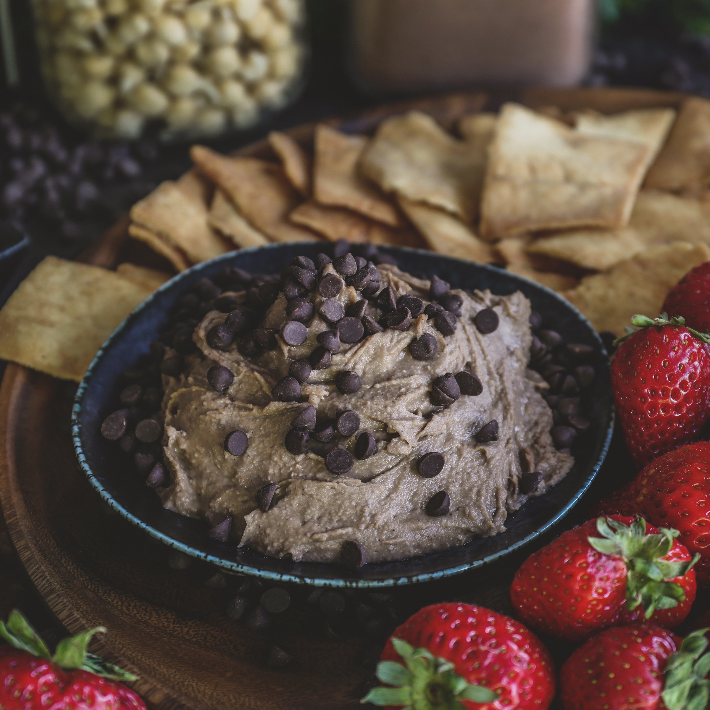 Bowl of chocolate hummus surrounded by pita crisps and strawberries. 