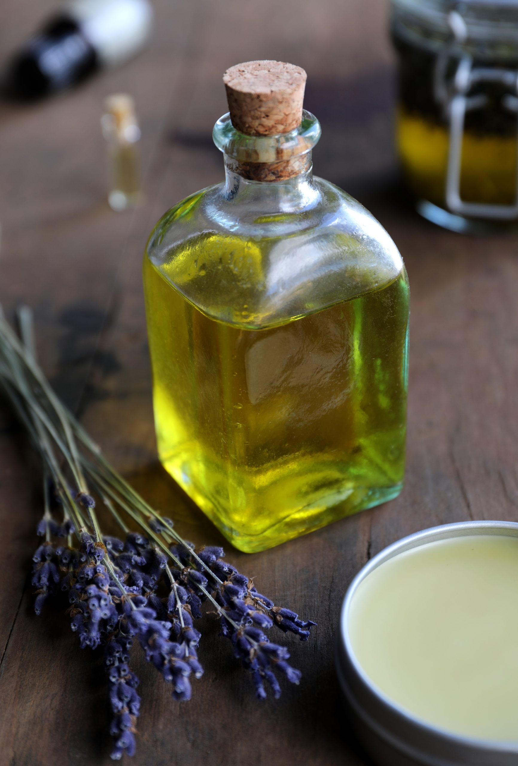 Vintage cork top glass bottle with oil in it with lavender and salve displayed in background.