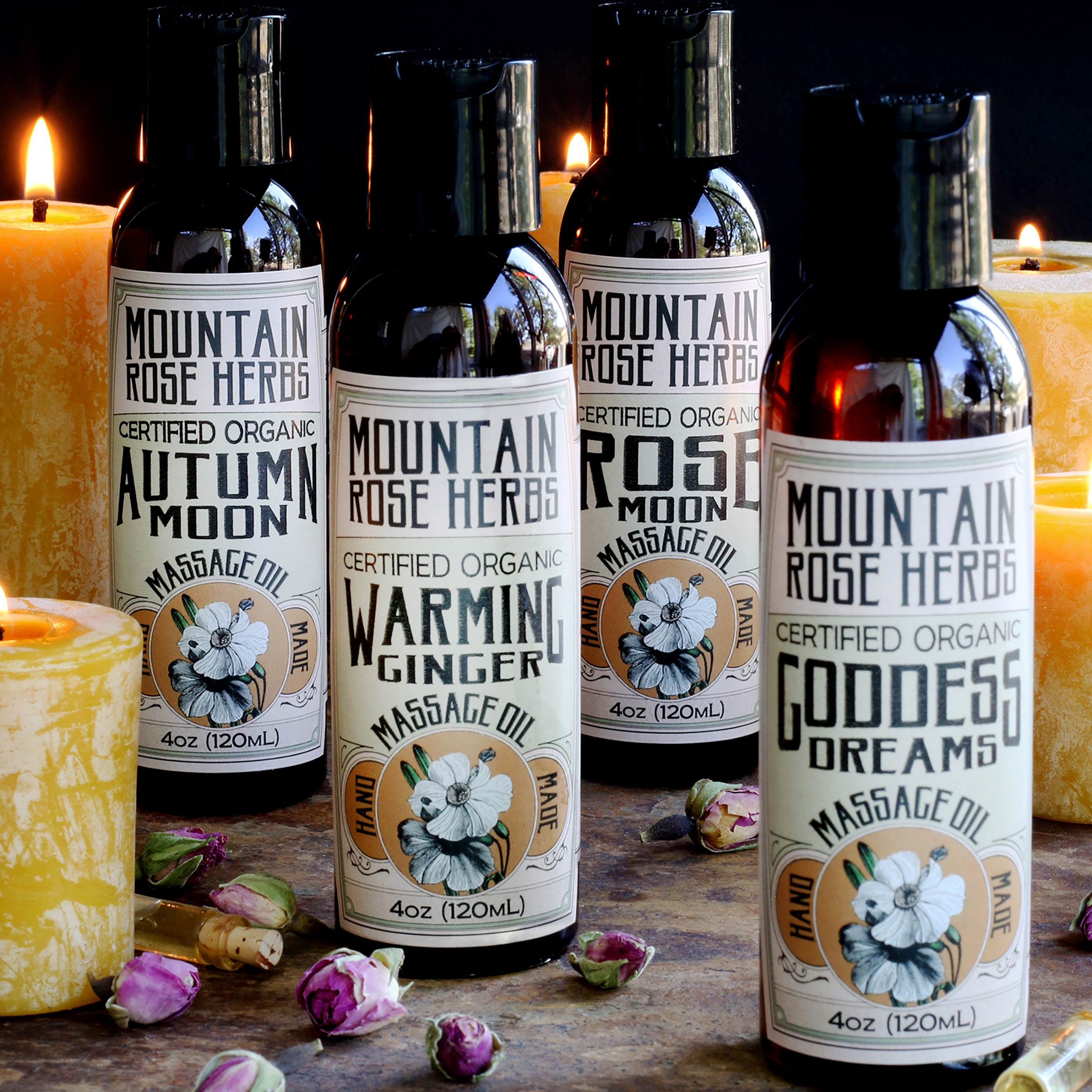 Natural and organic massage oil collection arrange with beeswax candles and dried rose buds. Four natural massage oil varieties from Mountain Rose Herbs.