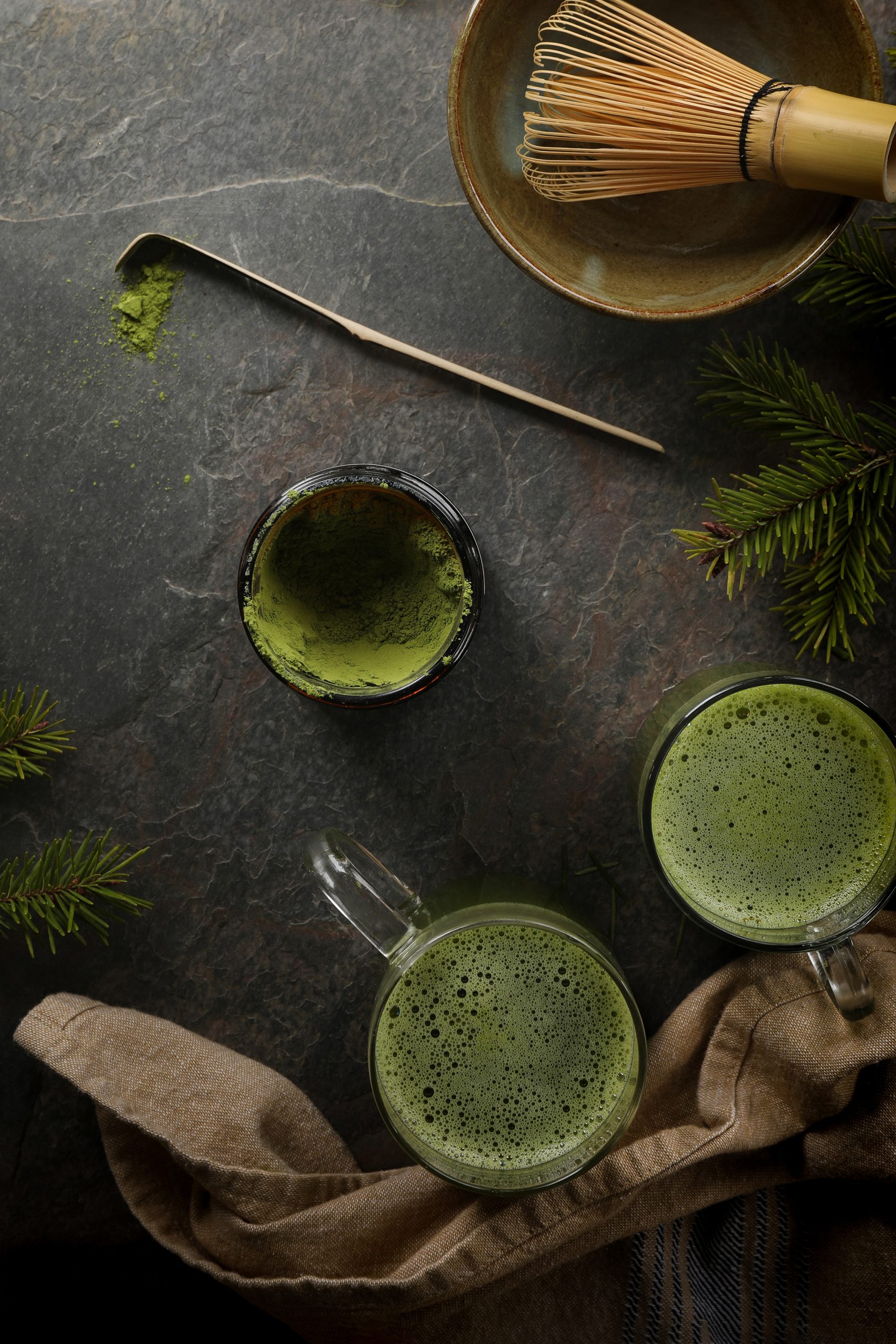 Frothy cups of matcha green tea are prepared using a bamboo matcha whisk and bamboo matcha spoon.