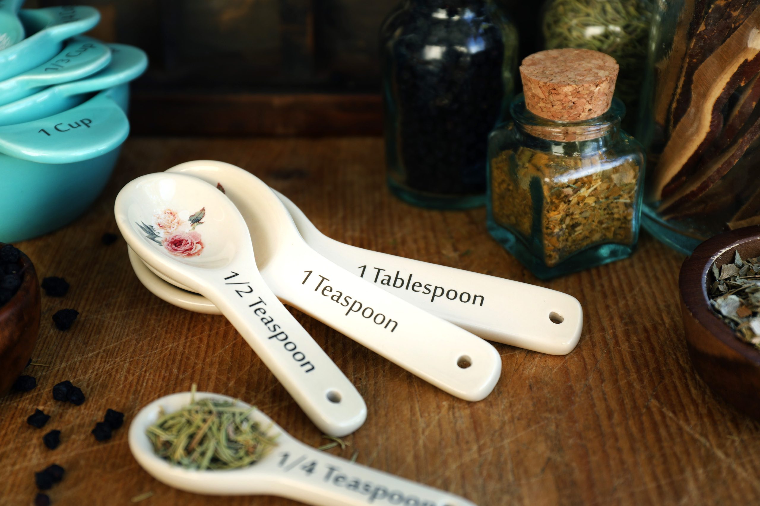 Fancy vintage measuring spoons are adorned with painted flowers and used to add organic rosemary leaf into herbal formulas by parts.