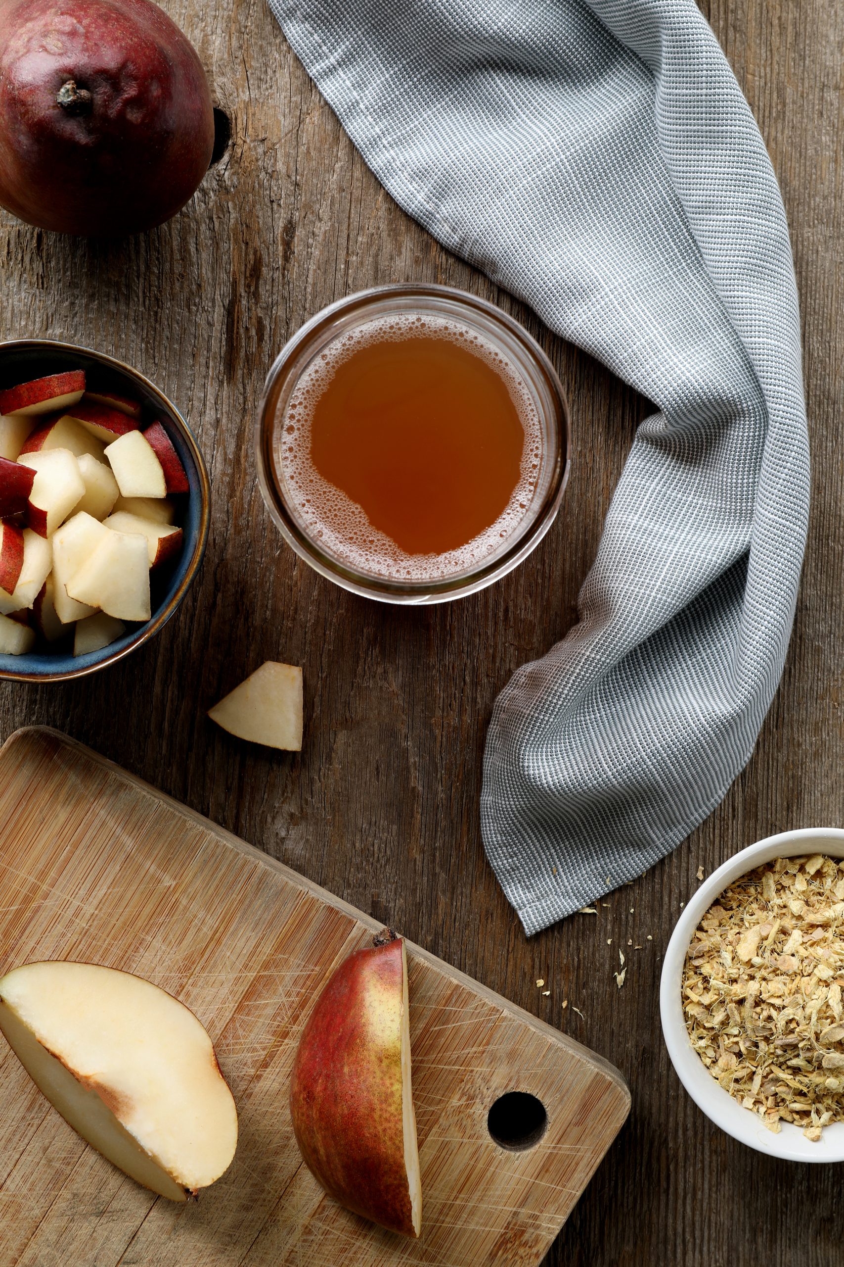 Pear-flavored kombucha arranged with fresh cut pears and dried ginger root on a rustic table top. 