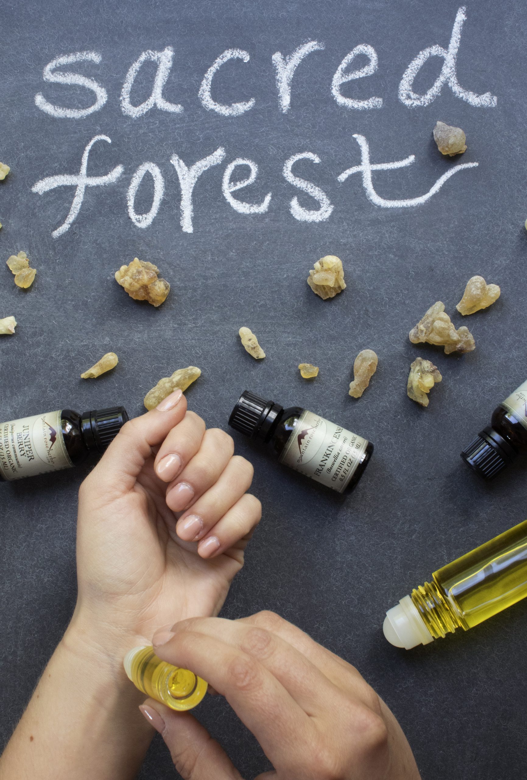 Person using roll on to apply perfume oil to wrists with essential oil bottles artfully displayed around. 