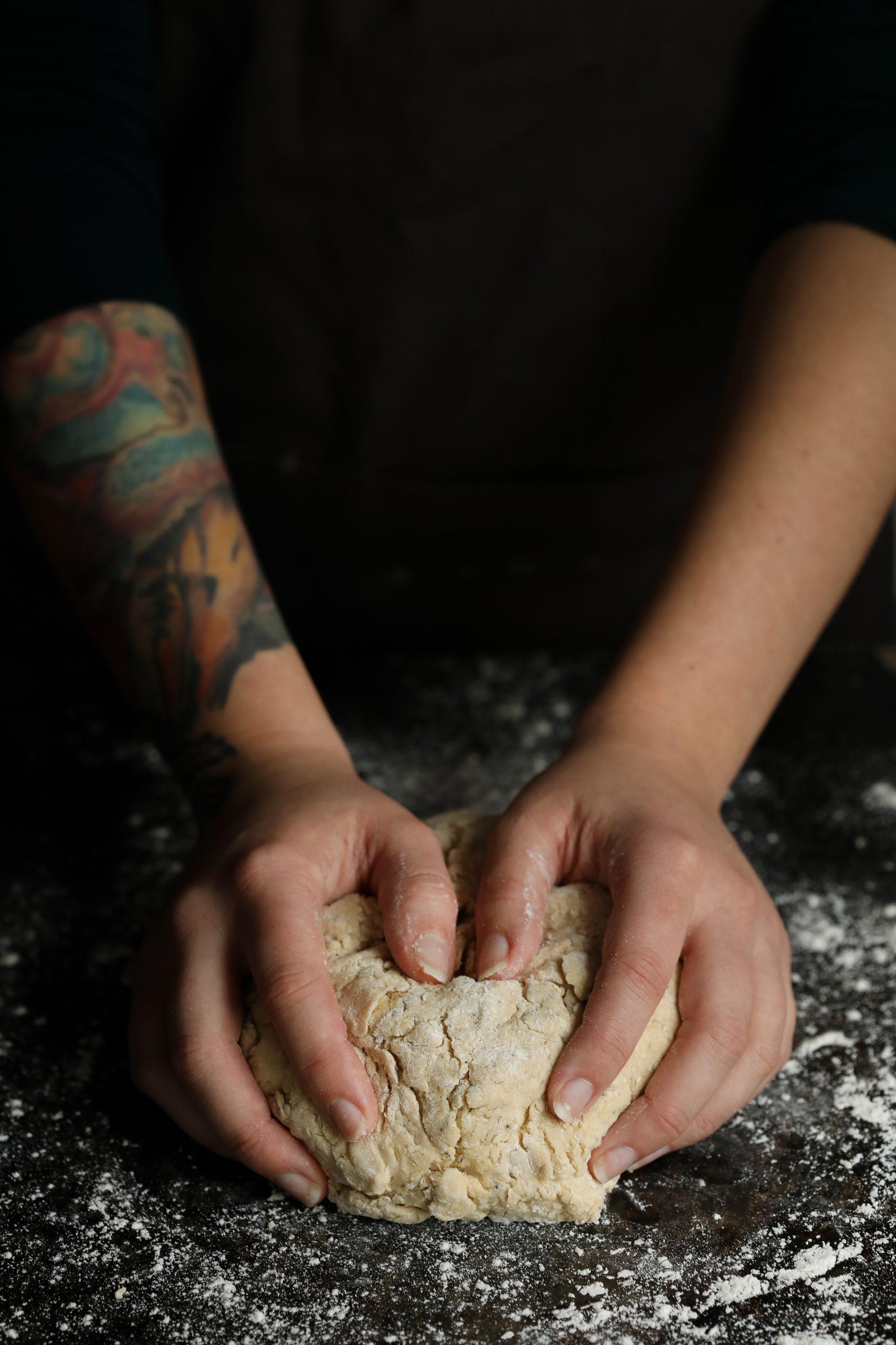 Kneading dough for Irish soda bread on a black tabletop sprinkled with flour. 