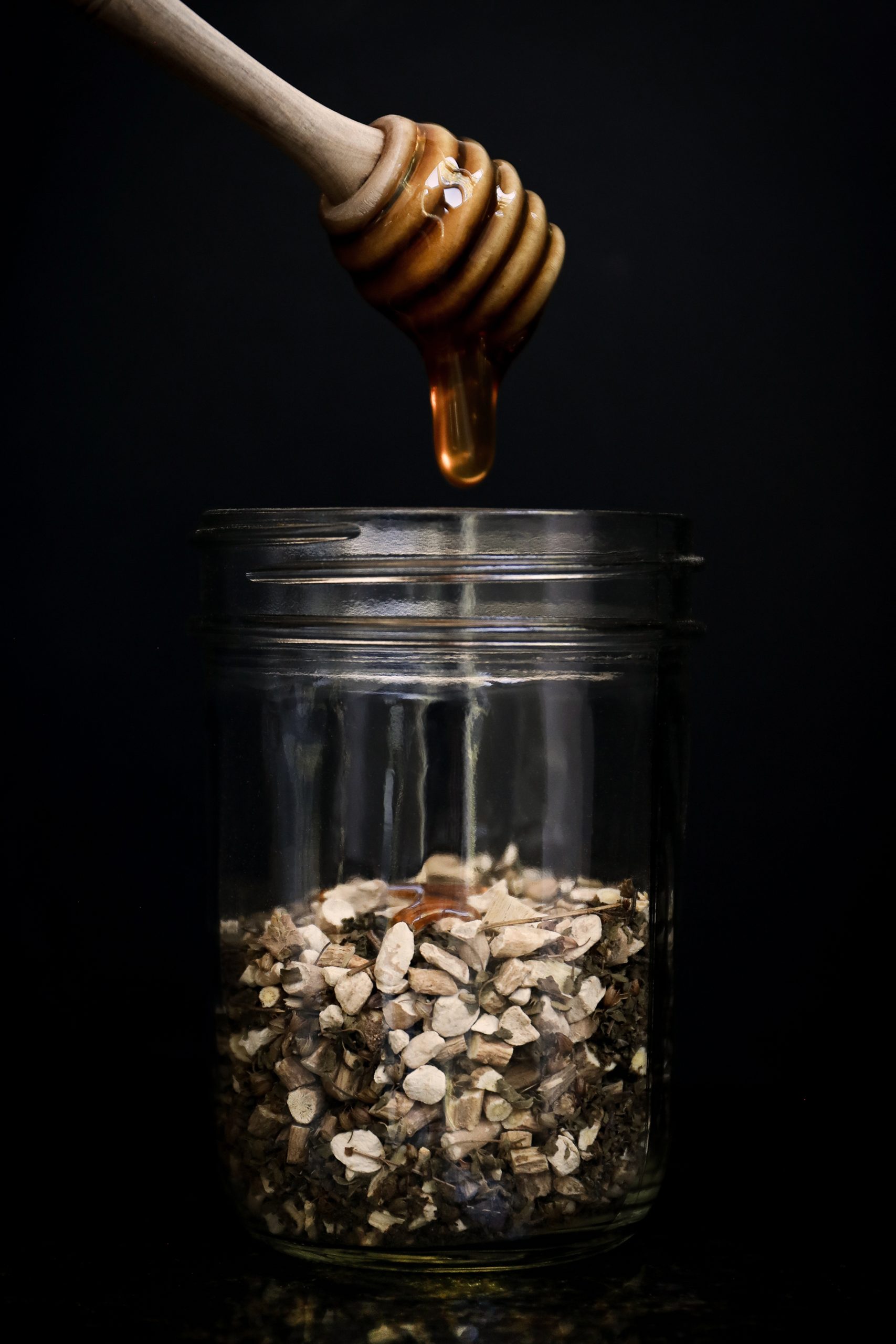 Holy basil, ashwagandha, and astragalus roots in a jar with honey drizzling over to make herbal elixir for stress relief.