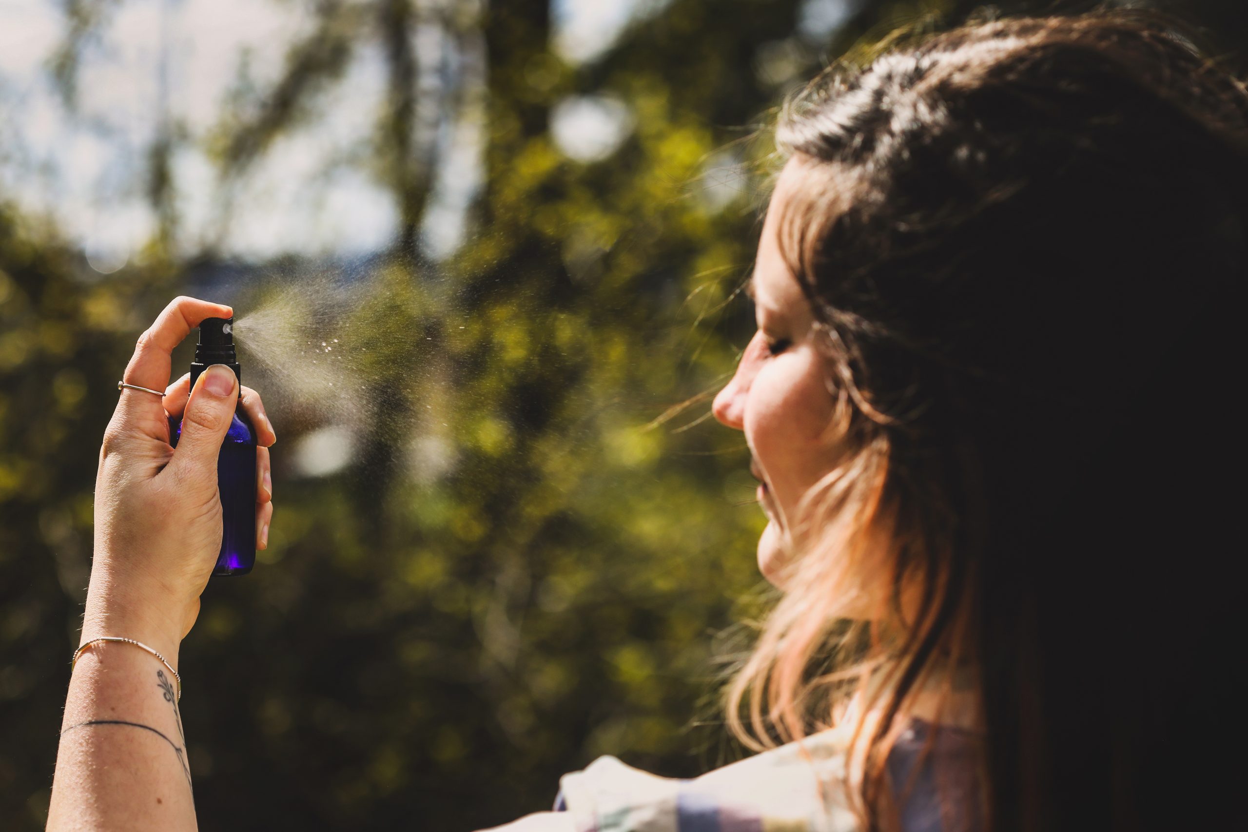 A woman misting herself with a diy peppermint and green tea cooling mist.