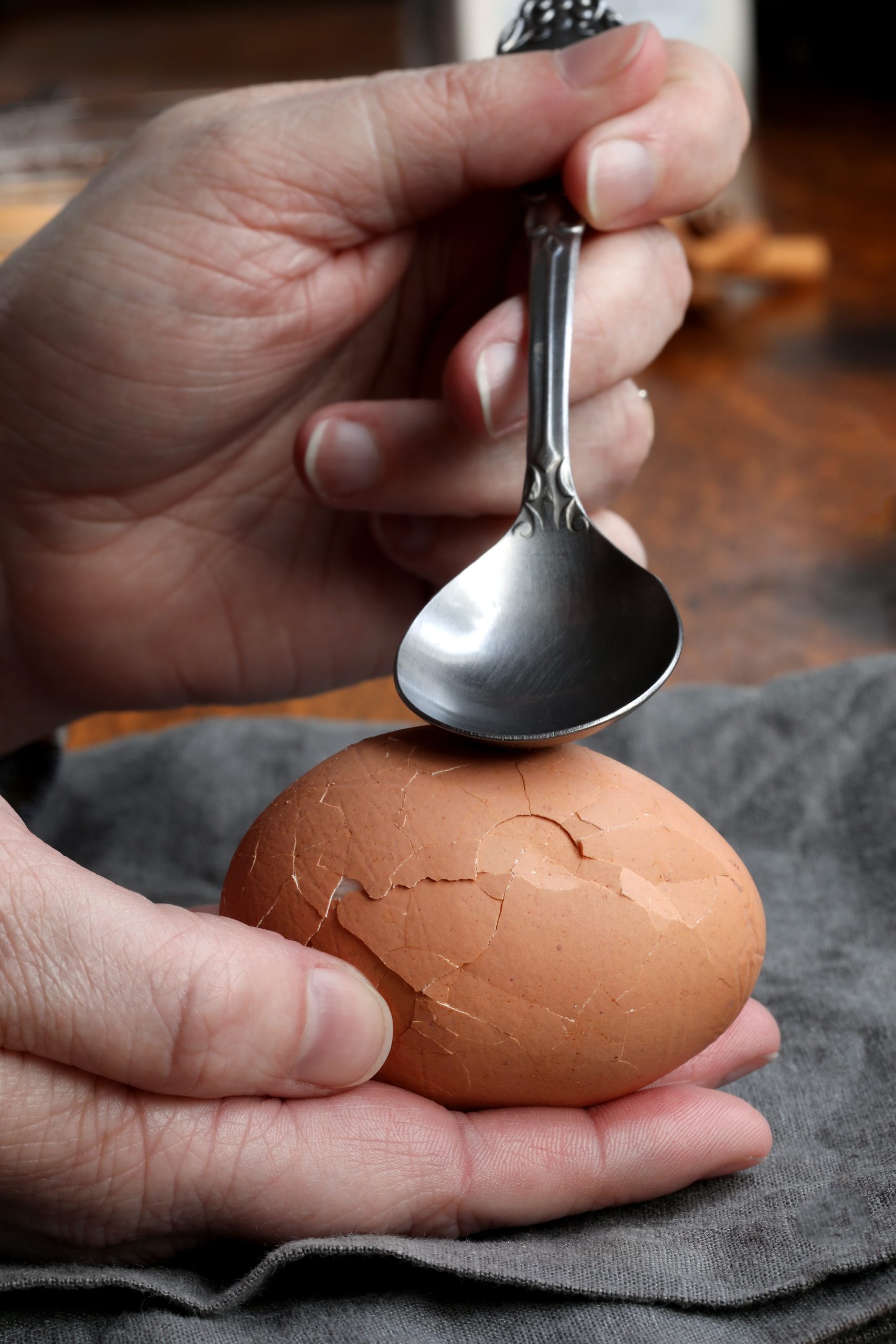 Hand holding spoon using utensil to crack marbled tea egg in palm of hand Hand holding spoon using utensil to crack marbled tea egg in palm of hand