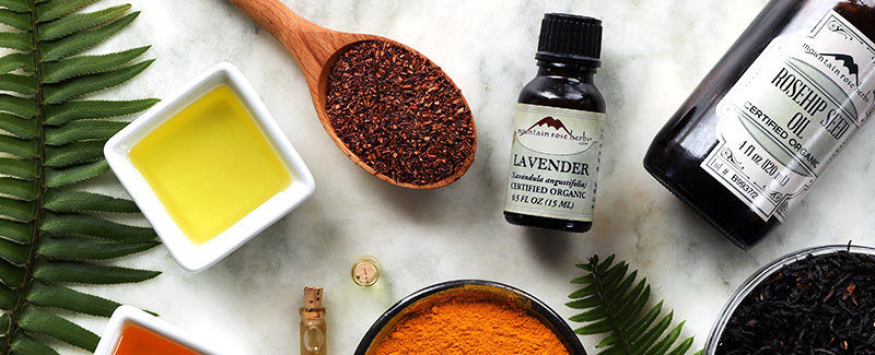 Colorful herbs, spices, oils, and other ingredients arrayed on marble with ferns sprinkled around.