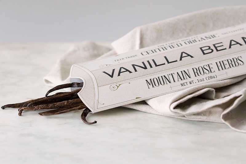 Rectangular paper package holding a bundle of vanilla beans lying on counter with fabric Rectangular paper package holding a bundle of vanilla beans lying on counter with fabric
