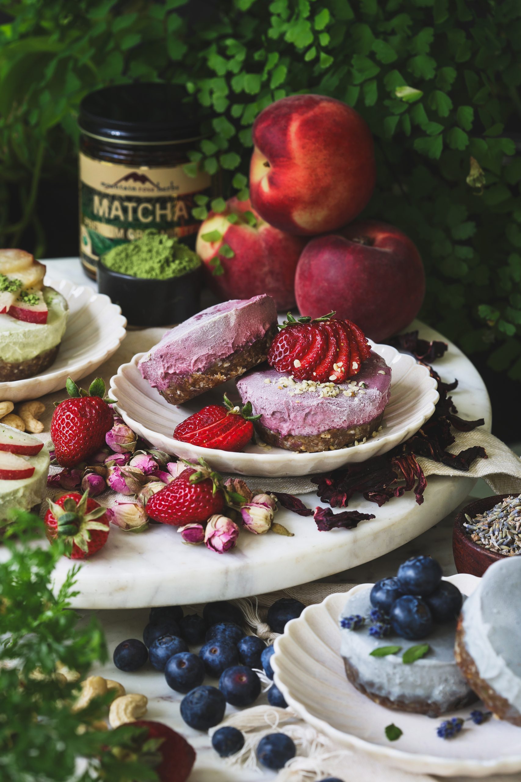 Vegan mini cheesecakes topped with fruit on three plates surrounded with ingredients