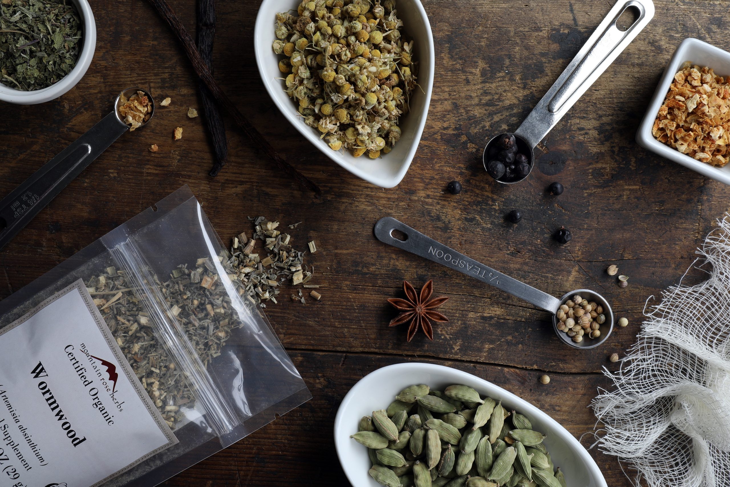 Ingredients for making homemade vermouth laying in bowls on counter including cardamom and wormwood and orange peel Ingredients for making homemade vermouth laying in bowls on counter including cardamom and wormwood and orange peel