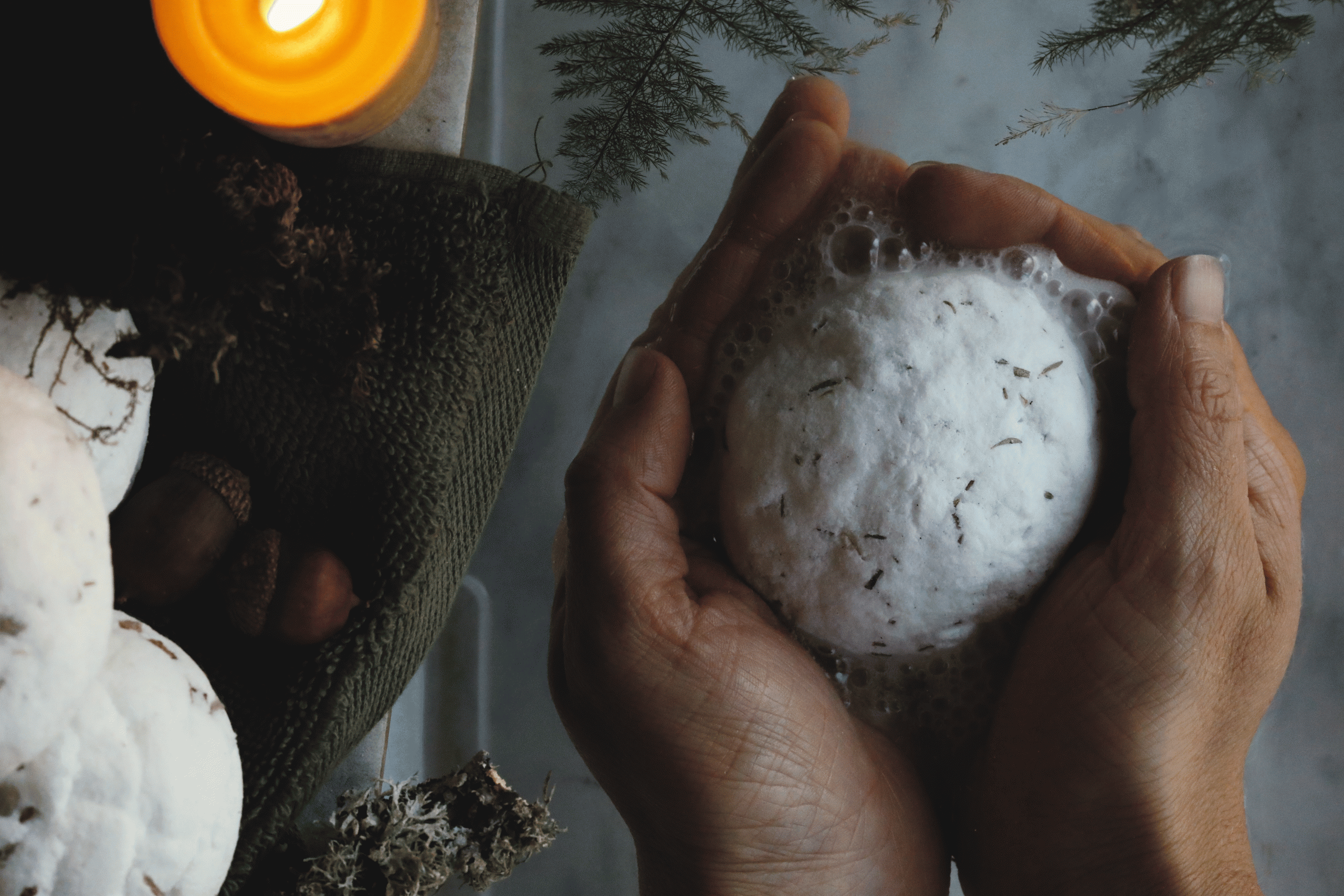 Hands holding a fizzing homemade bath bomb in water.