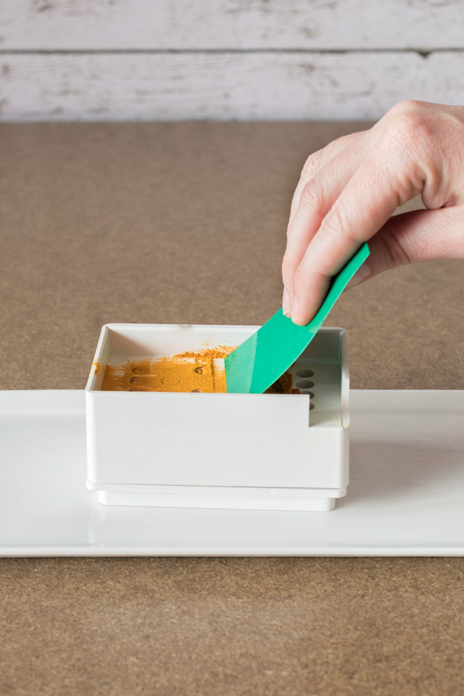 Using the spreader card to evenly distribute the organic turmeric powder into the capsule machine base