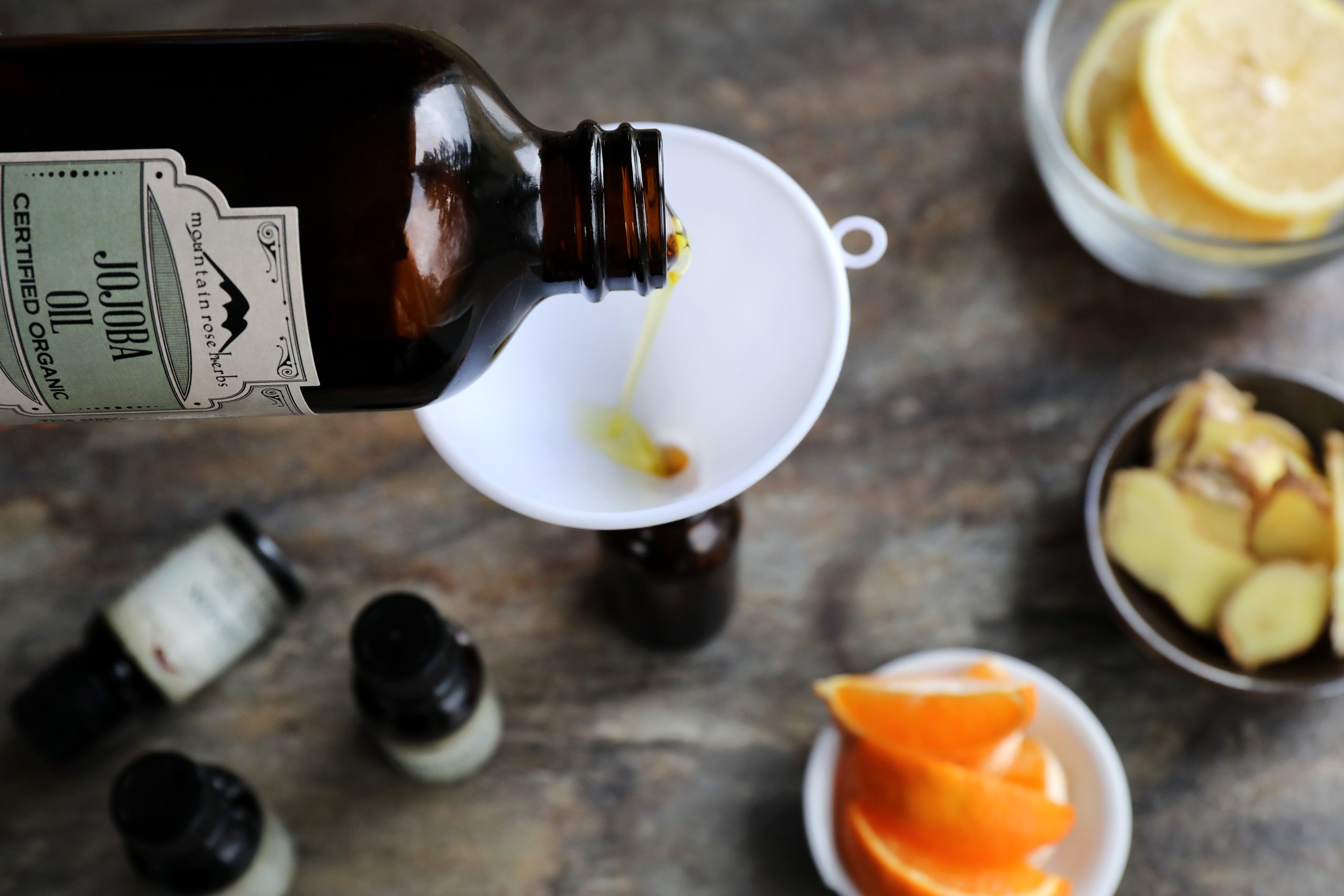 Bottle of Jojoba oil being poured through a funnel into a glass bottle with essential oils bottles around.