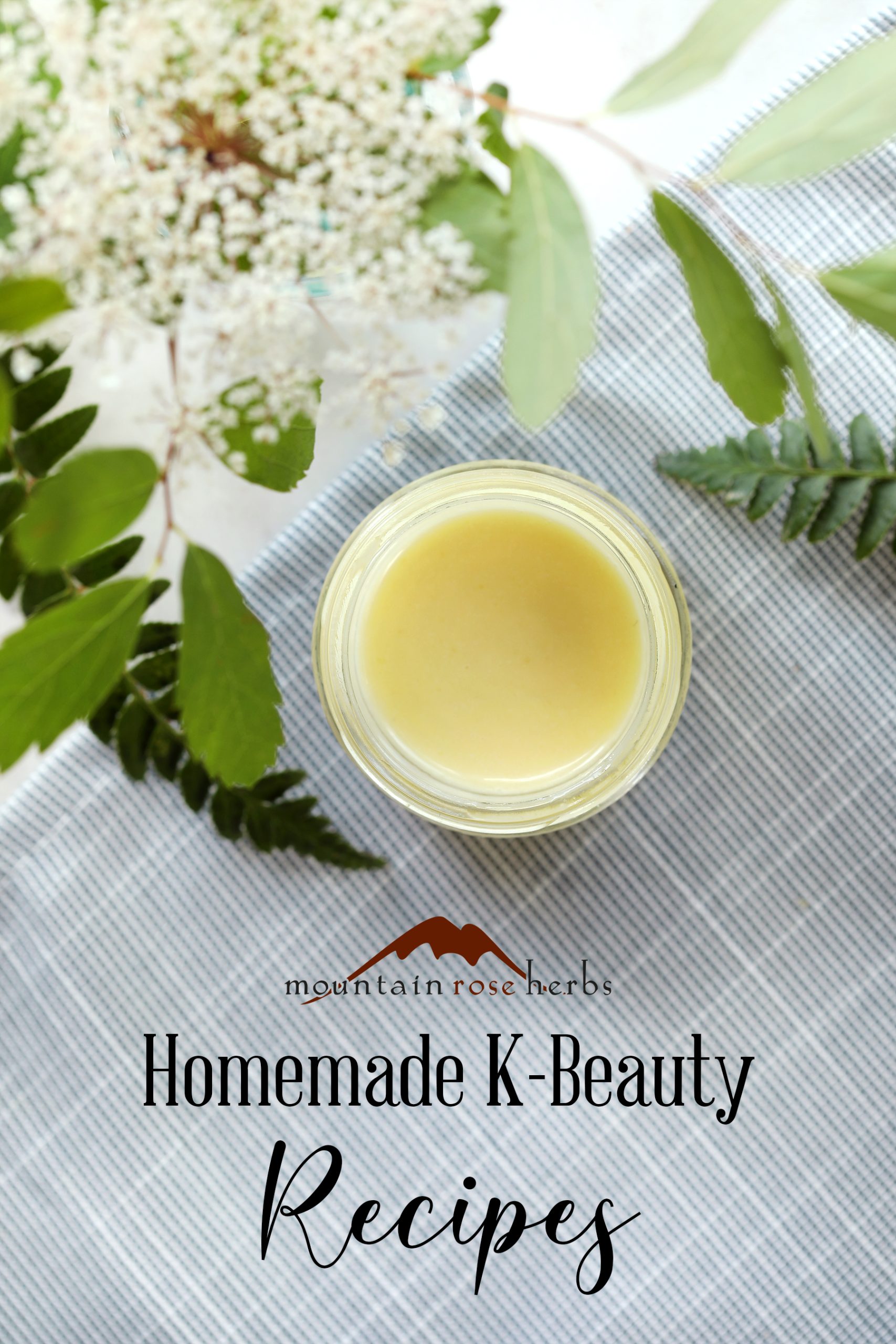 Pinterest link to Mountain Rose Herbs. Finished propolis and chamomile skin cream emulsion is arranged with fresh foliage and a blue serviette on a marble counter top.