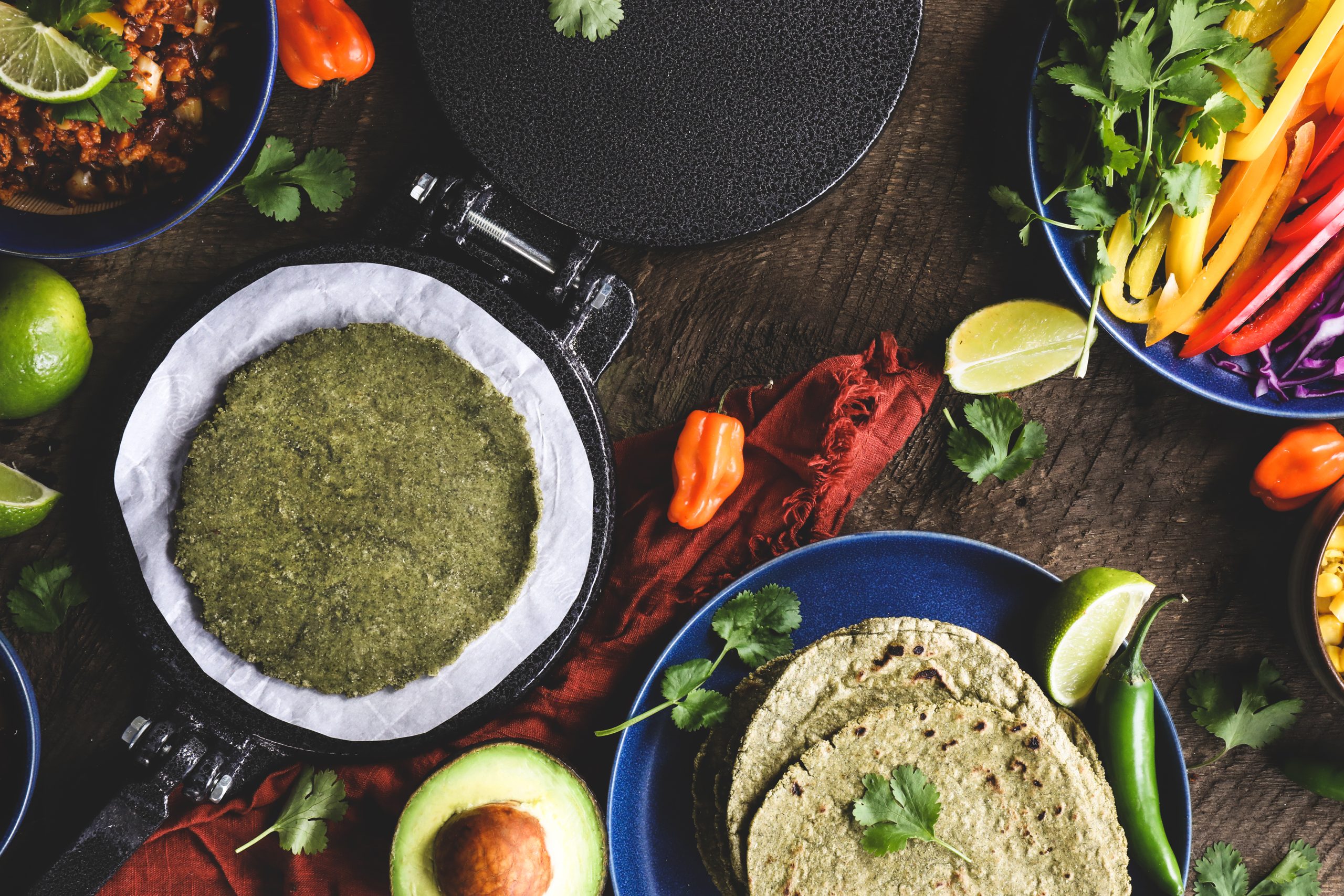 Raw green torilla in press surrounded by fresh ingredients. 