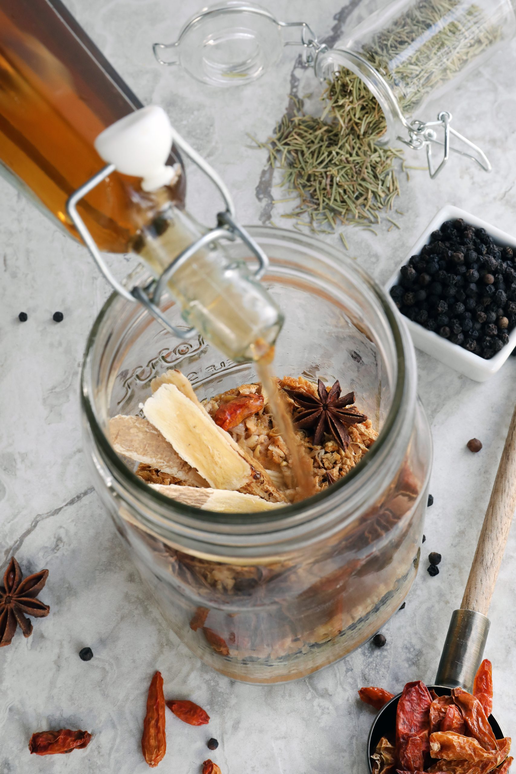 Bottle of apple cider vinegar being poured into mason jar of colorful spices.
