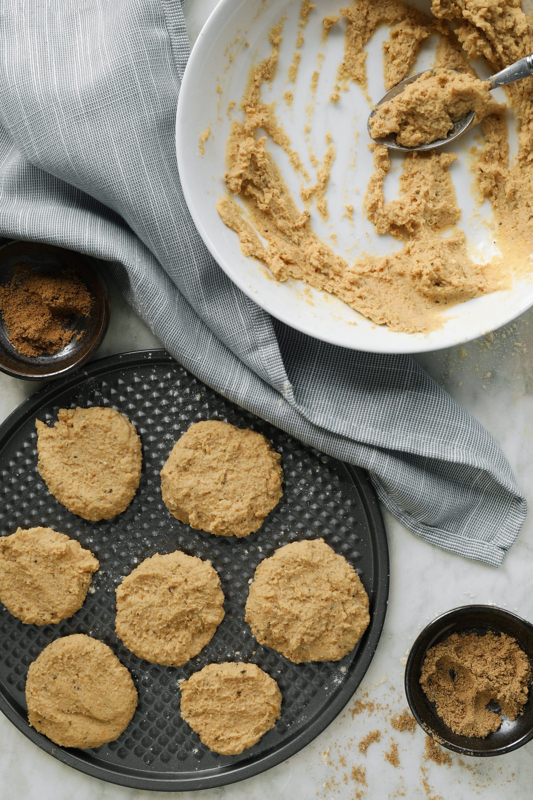 Hand formed falafel patties arranged on a baking tray. Falafel mix of chickpeas and spices including coriander, cumin, and black pepper.
