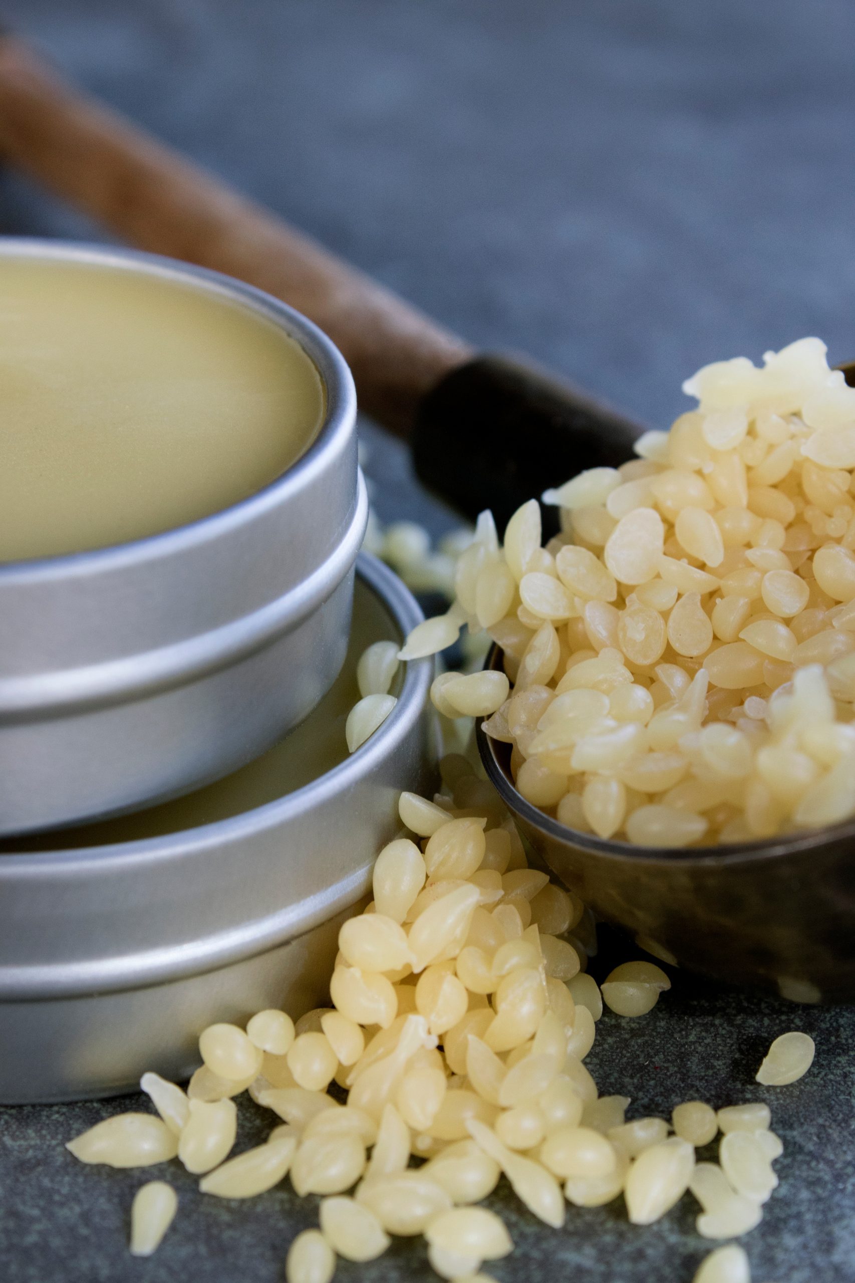 Tins filled with salve, spoon with beeswax pastilles spilling out. 