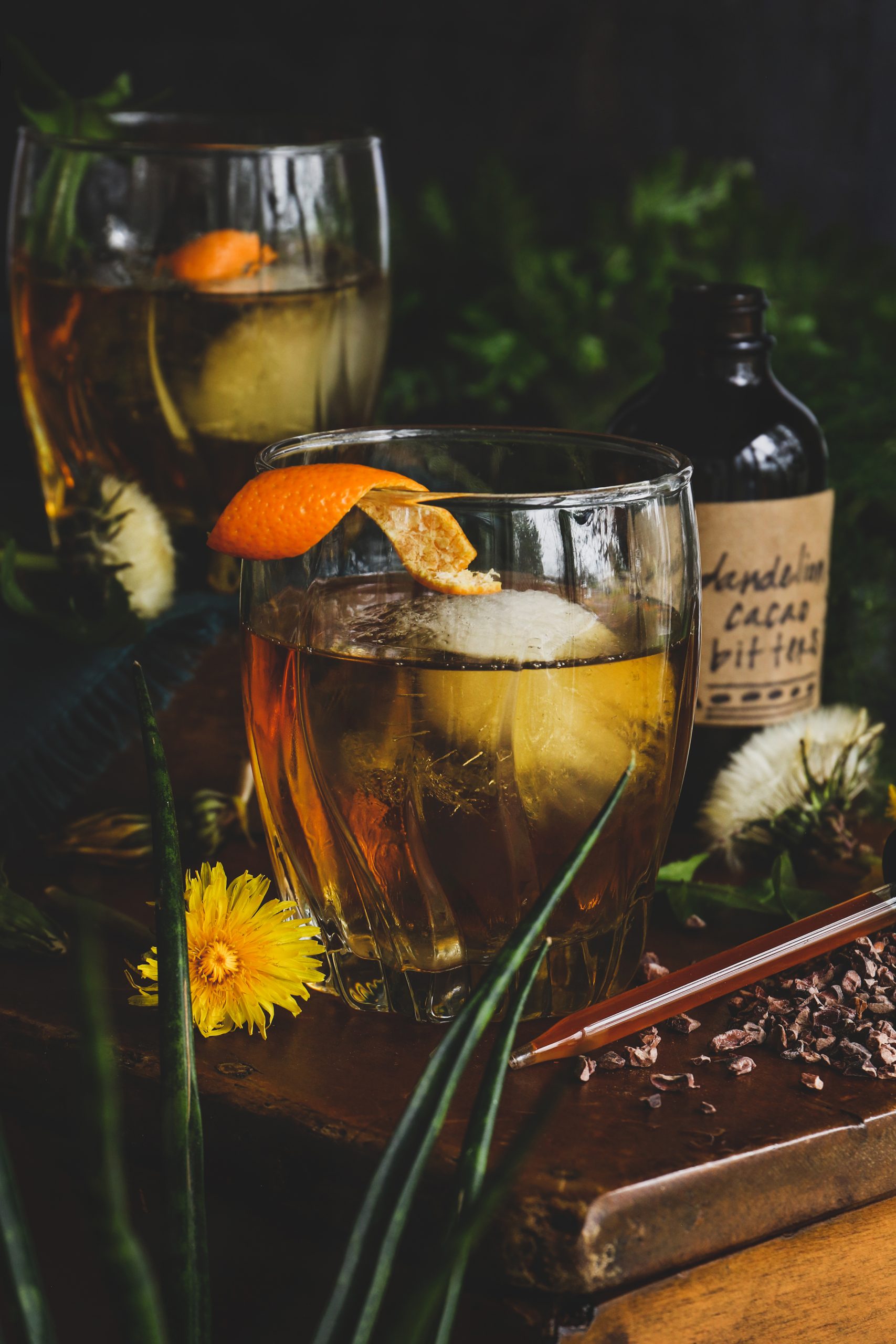Photo of a cocktail glass with large ice cube and a fresh orange peel garnish.