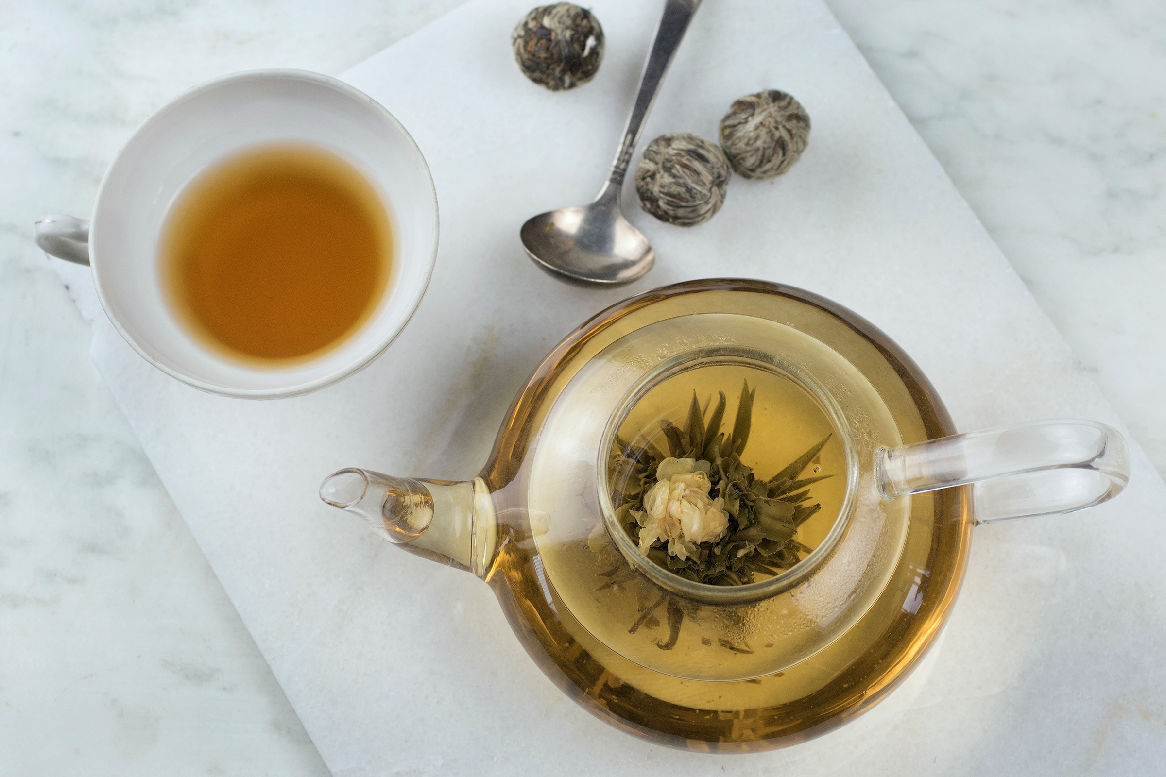 Glass teapot with brewed flowering tea, teacup with brewed green tea, cutting board