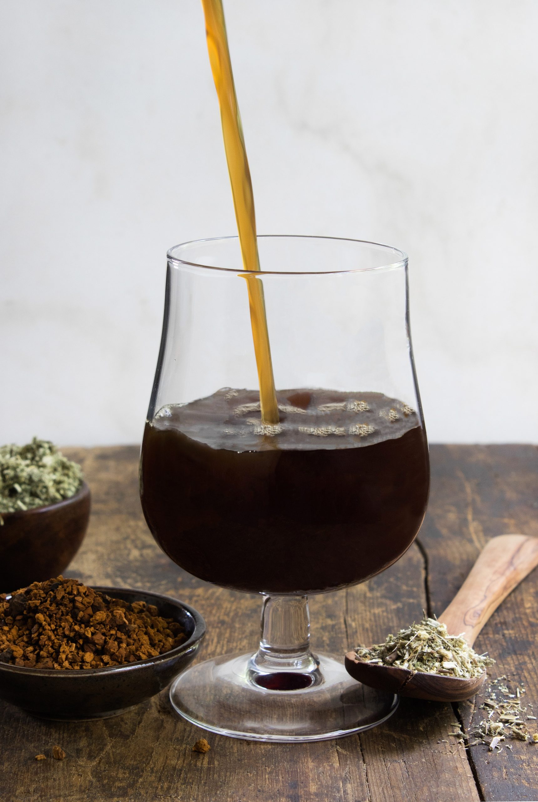 Deep roots gruit (herbal beer) being poured into a glass next to herbs and mushrooms used for brew