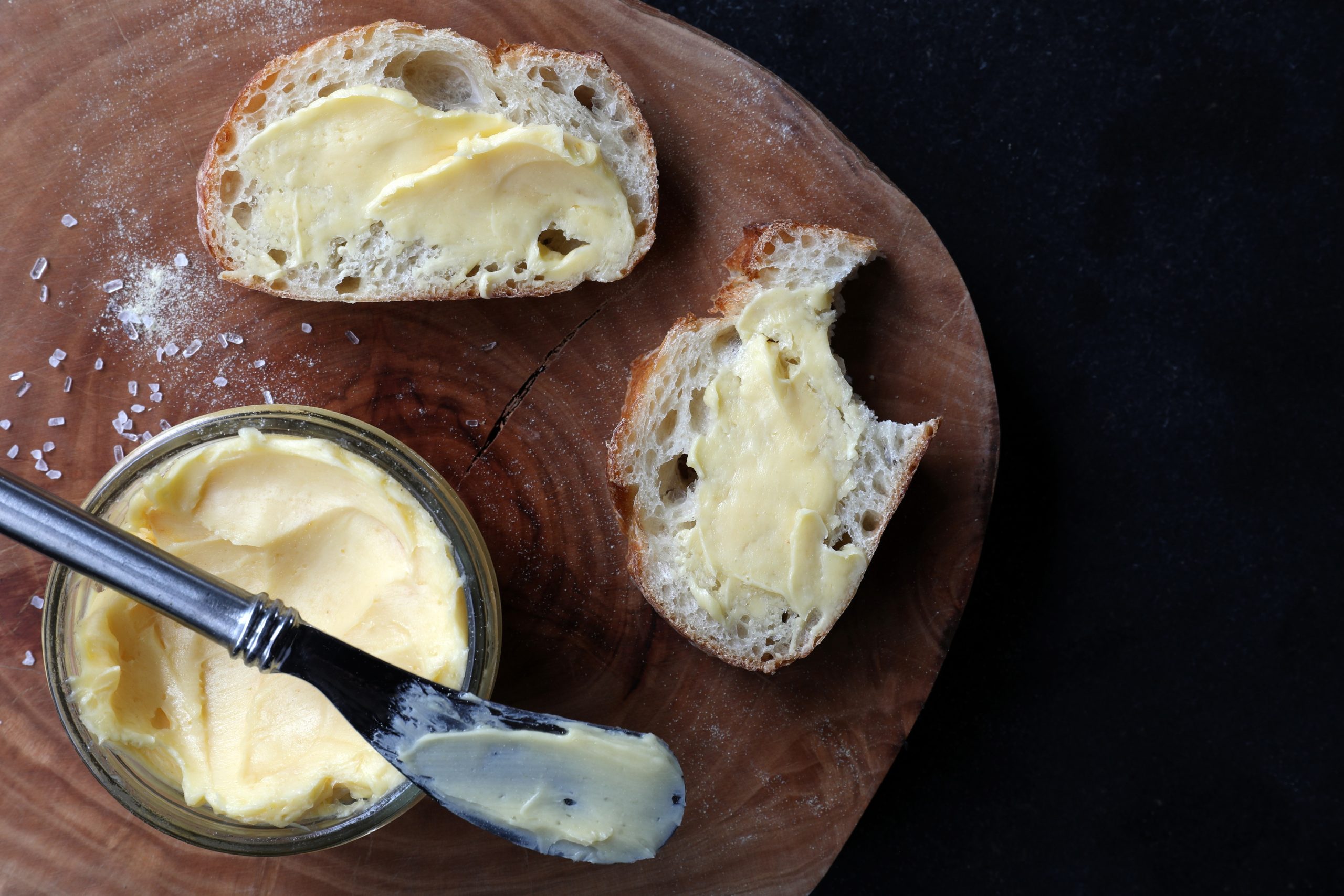 Slices of bread with garlic butter on cutting board next to glass jar of butter. 