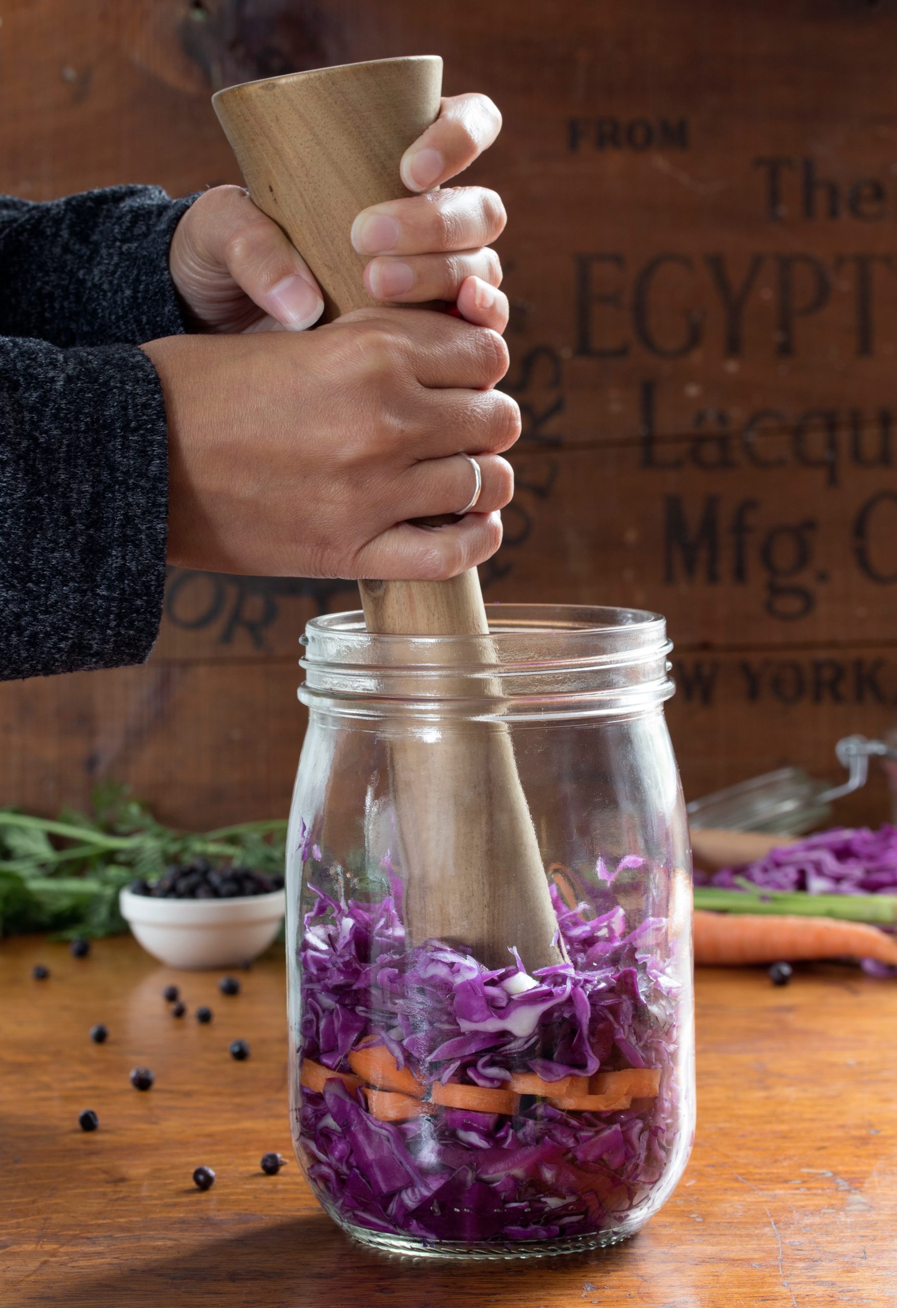 Hands using wooden pestle to massage cabbage to make sauerkraut in a glass jar Hands using wooden pestle to massage cabbage to make sauerkraut in a glass jar