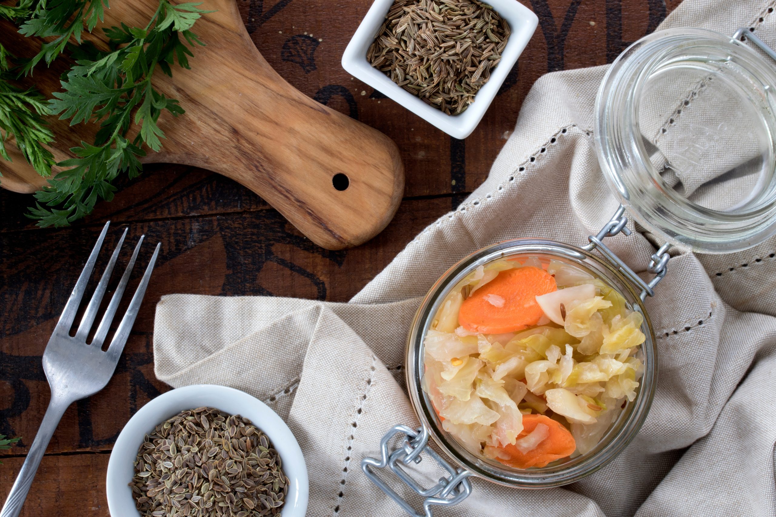 Glass jar of seeded sauerkraut with caraway seeds and mustard seeds with napkin and fork Glass jar of seeded sauerkraut with caraway seeds and mustard seeds with napkin and fork