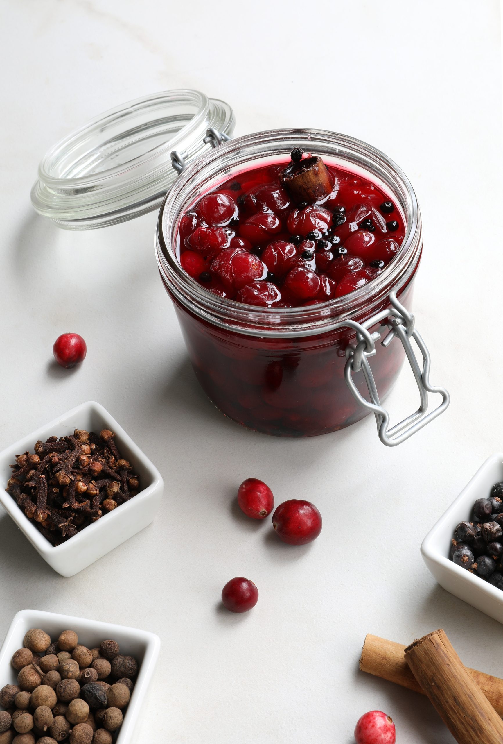 Canning Jar with pickled crannberries inside on counter with dried herbs and spices