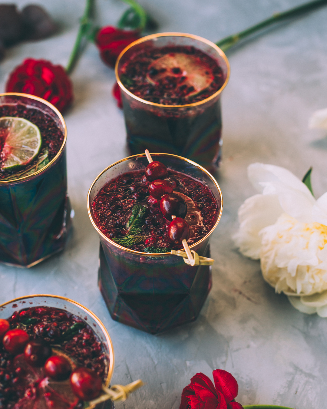 Holiday cocktails, or mocktails without alcohol, made with organic maqui berries and bilberries in trendy glass jars with gold rims and garnished with pomegranate seeds, fresh lime wheels, and cranberries.
