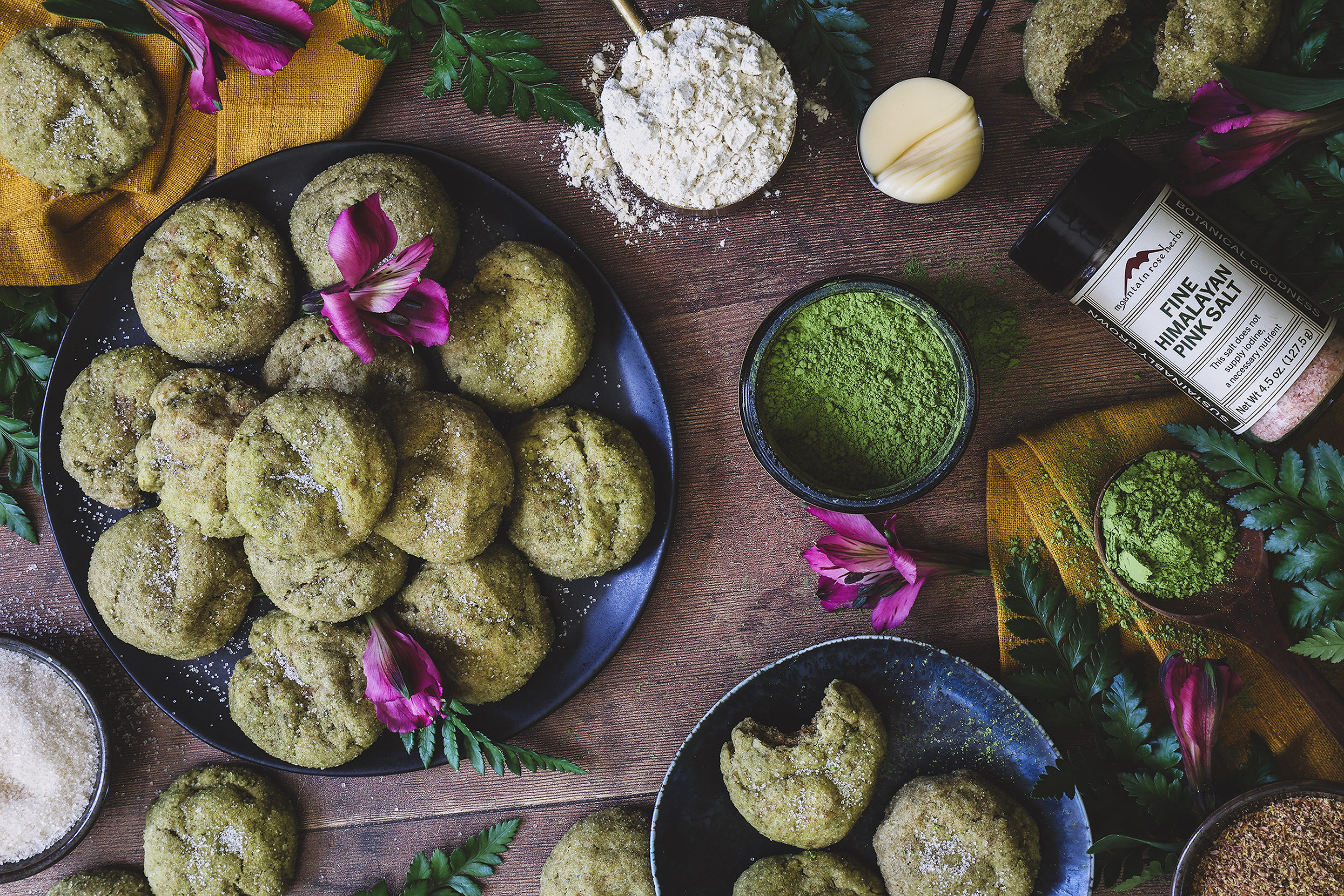 An overhead shot of matcha cookies on a plate with ingredients around it