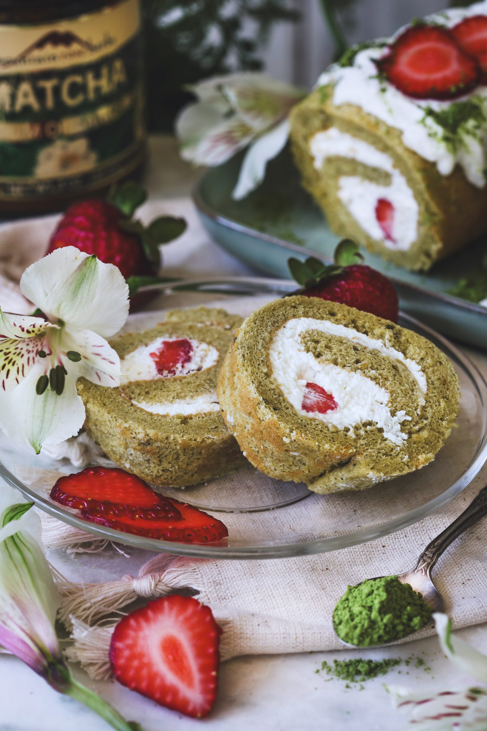 Matcha Swiss Roll Slices surrounded by fresh strawberries and matcha tea powder.