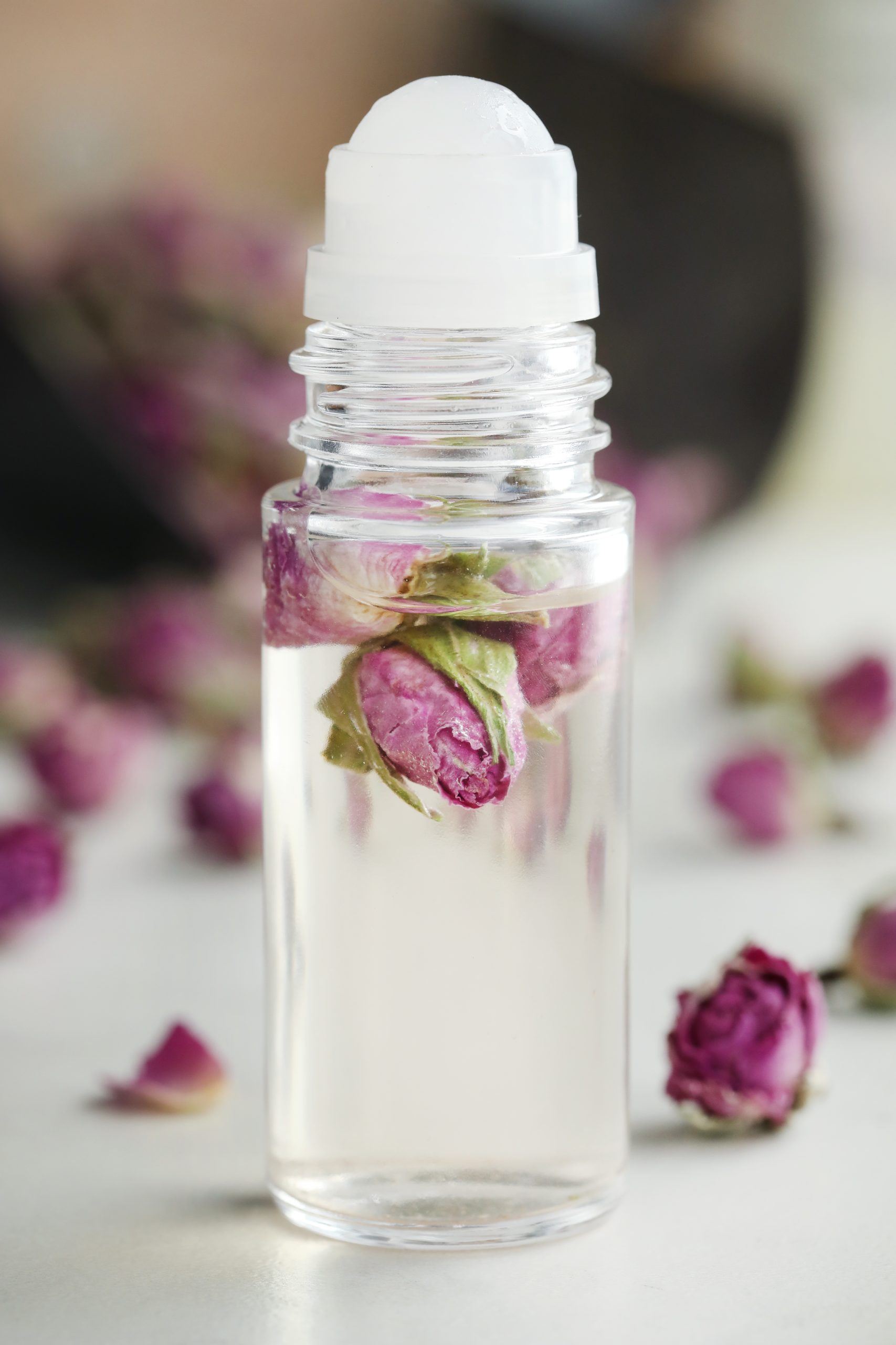Clear glass roll top perfume bottle with rose buds inside.