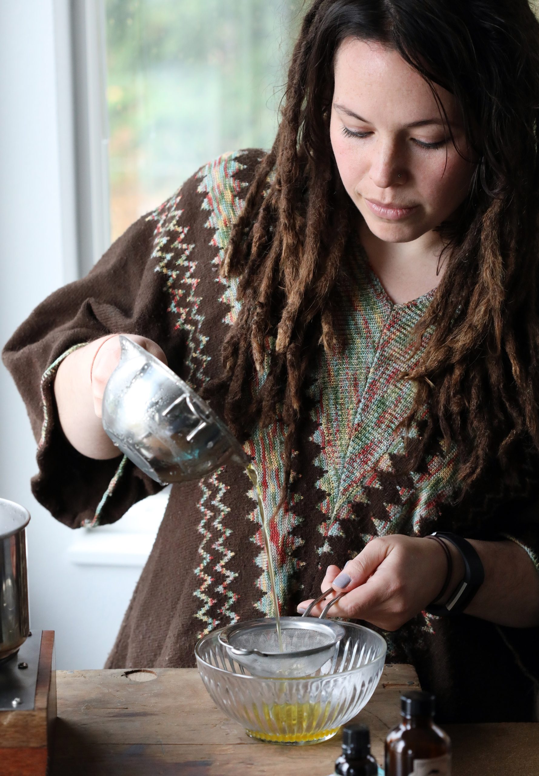 Person pouring oil from a double boiler through a strainer into a bowl. 